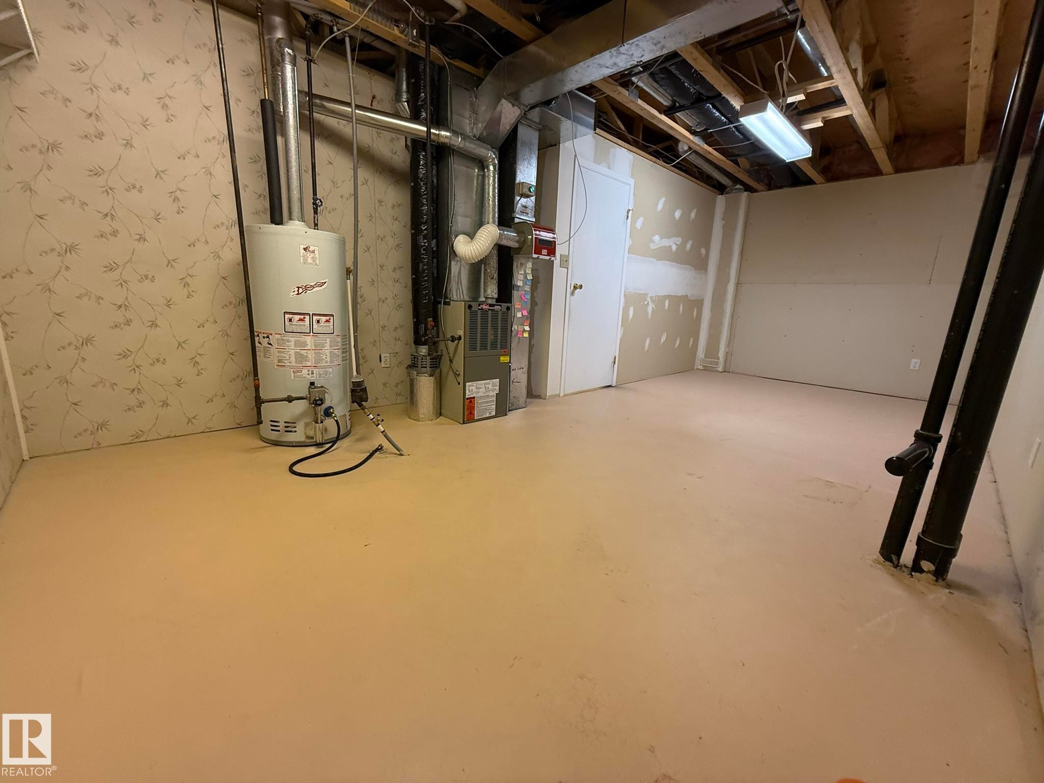 Utility room featuring a water heater, furnace, exposed overhead ductwork, and fluorescent lighting - 102 4610 50 Avenue, Stony Plain, AB