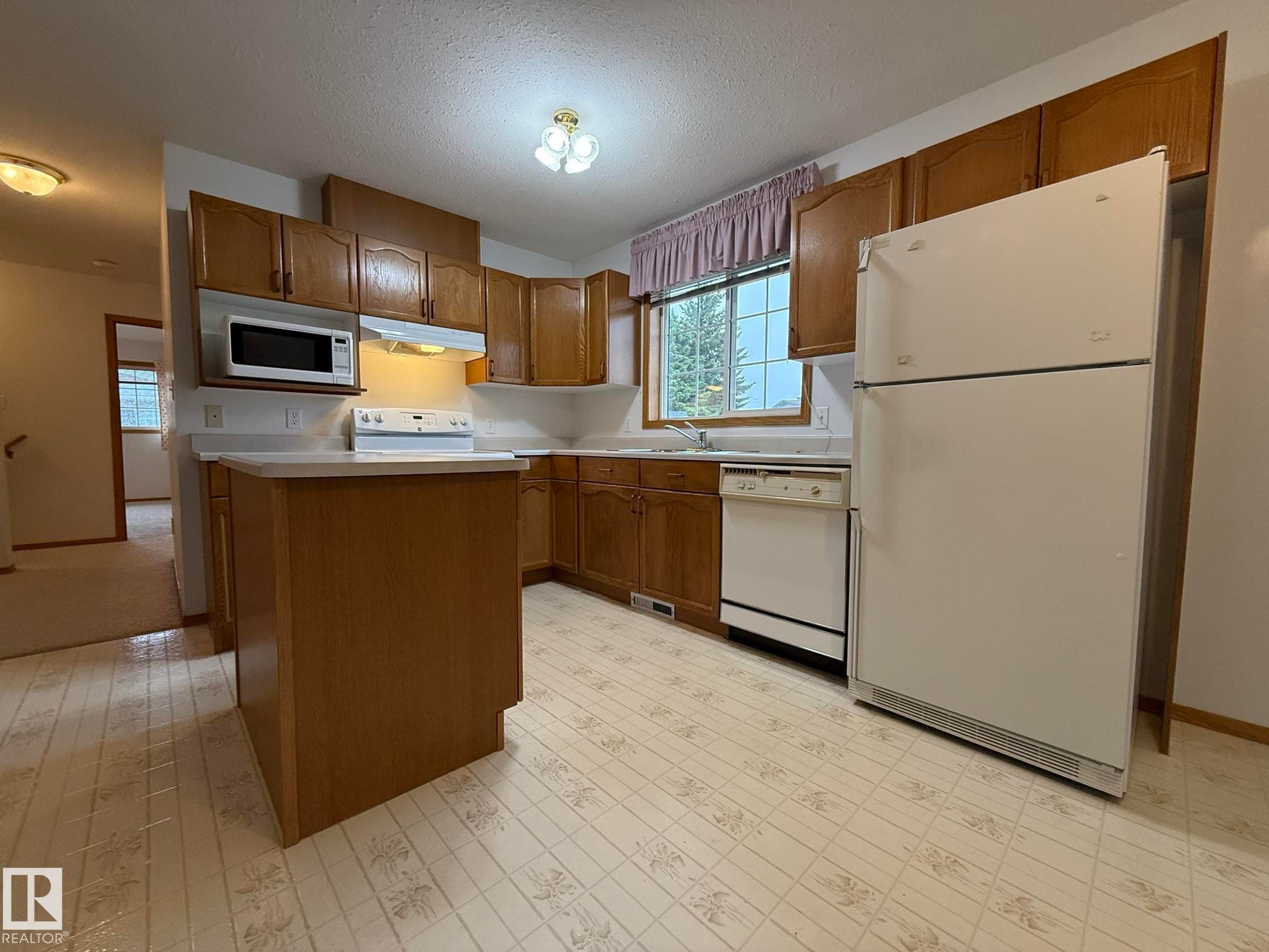 Kitchen with wood cabinetry, light countertops, and patterned vinyl flooring - 102 4610 50 Avenue, Stony Plain, AB
