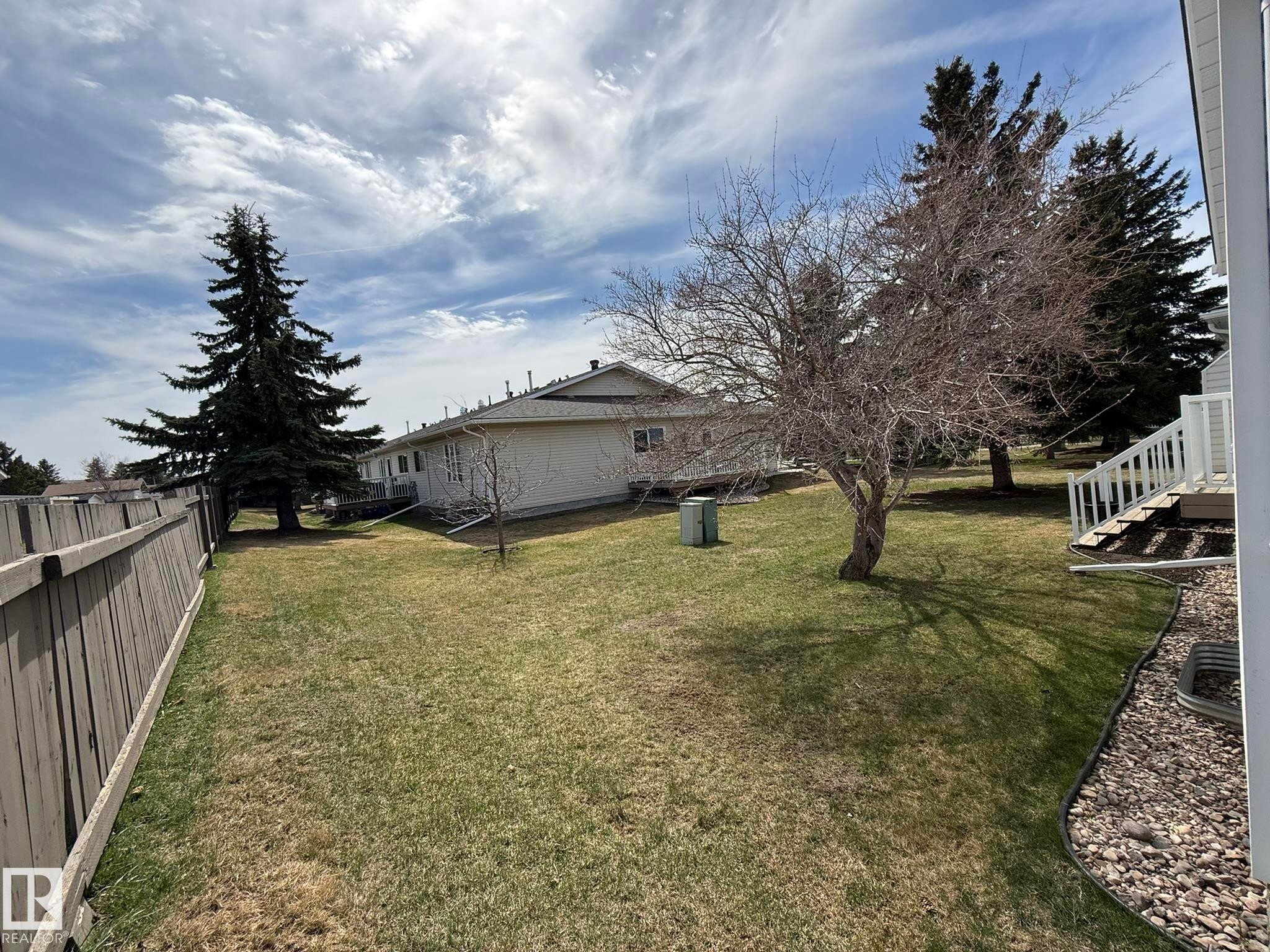 Expansive rear yard featuring a large mature conifer, established deciduous tree, manicured lawn, and wooden privacy fencing - 102 4610 50 Avenue, Stony Plain, AB