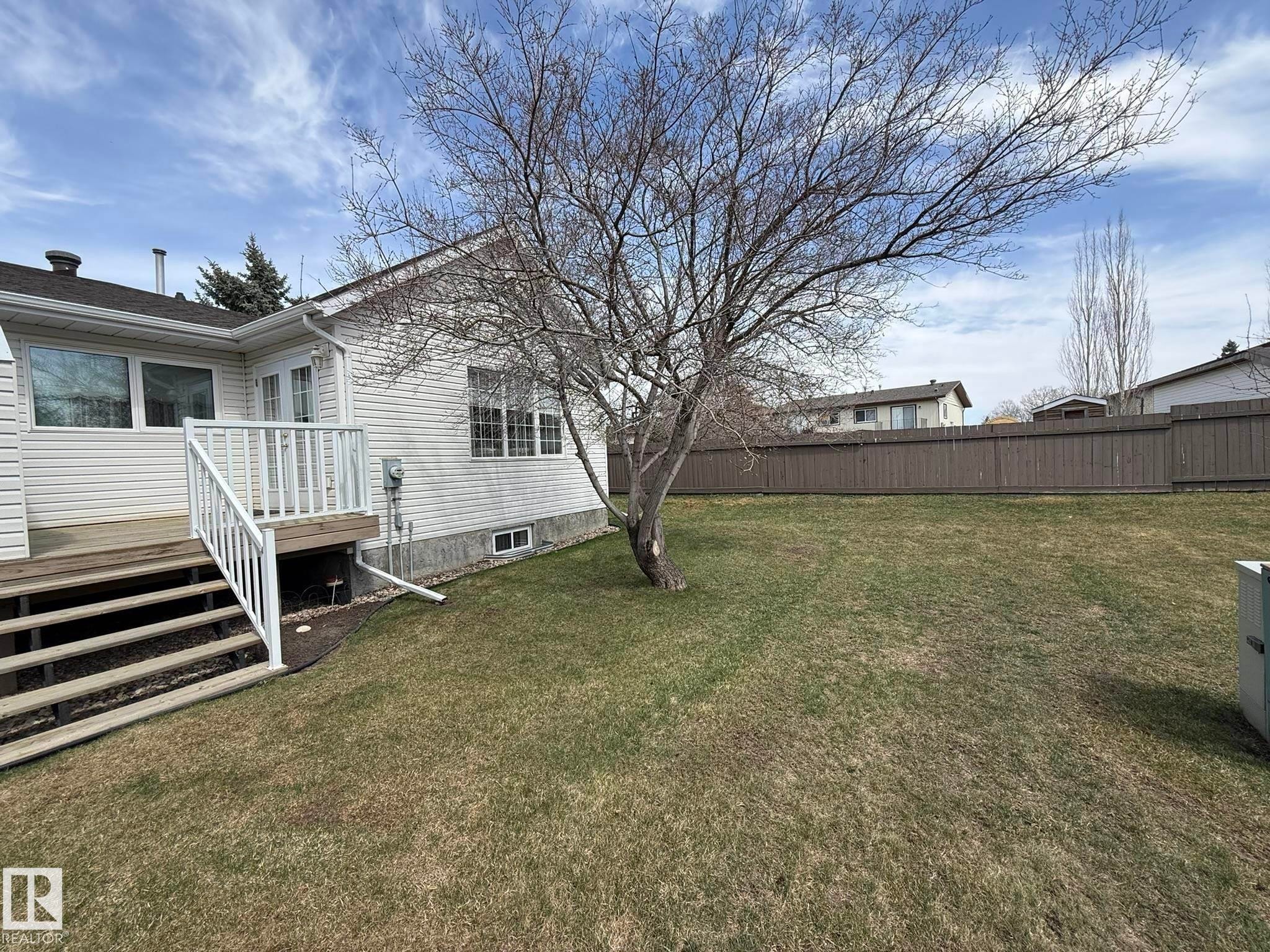 Spacious backyard featuring a wooden deck with white railings, a mature deciduous tree, and a wooden privacy fence - 102 4610 50 Avenue, Stony Plain, AB