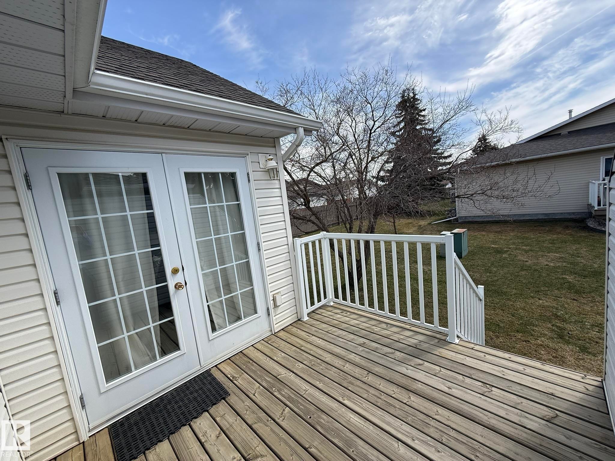Outdoor deck with wood-finish flooring, white railing, and white vinyl siding - 102 4610 50 Avenue, Stony Plain, AB