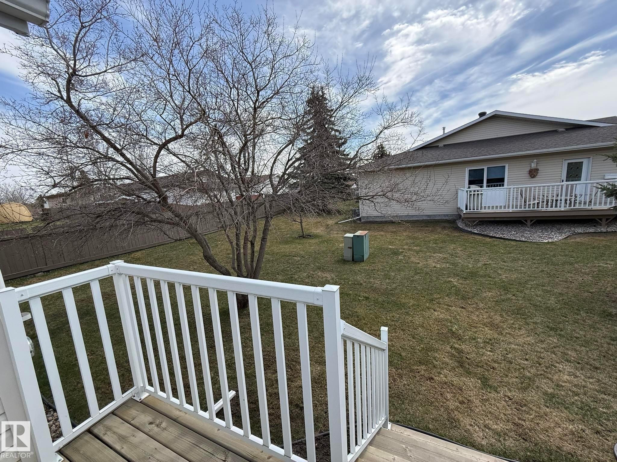 Spacious backyard featuring a sloped lawn, mature trees, and a privacy fence - 102 4610 50 Avenue, Stony Plain, AB