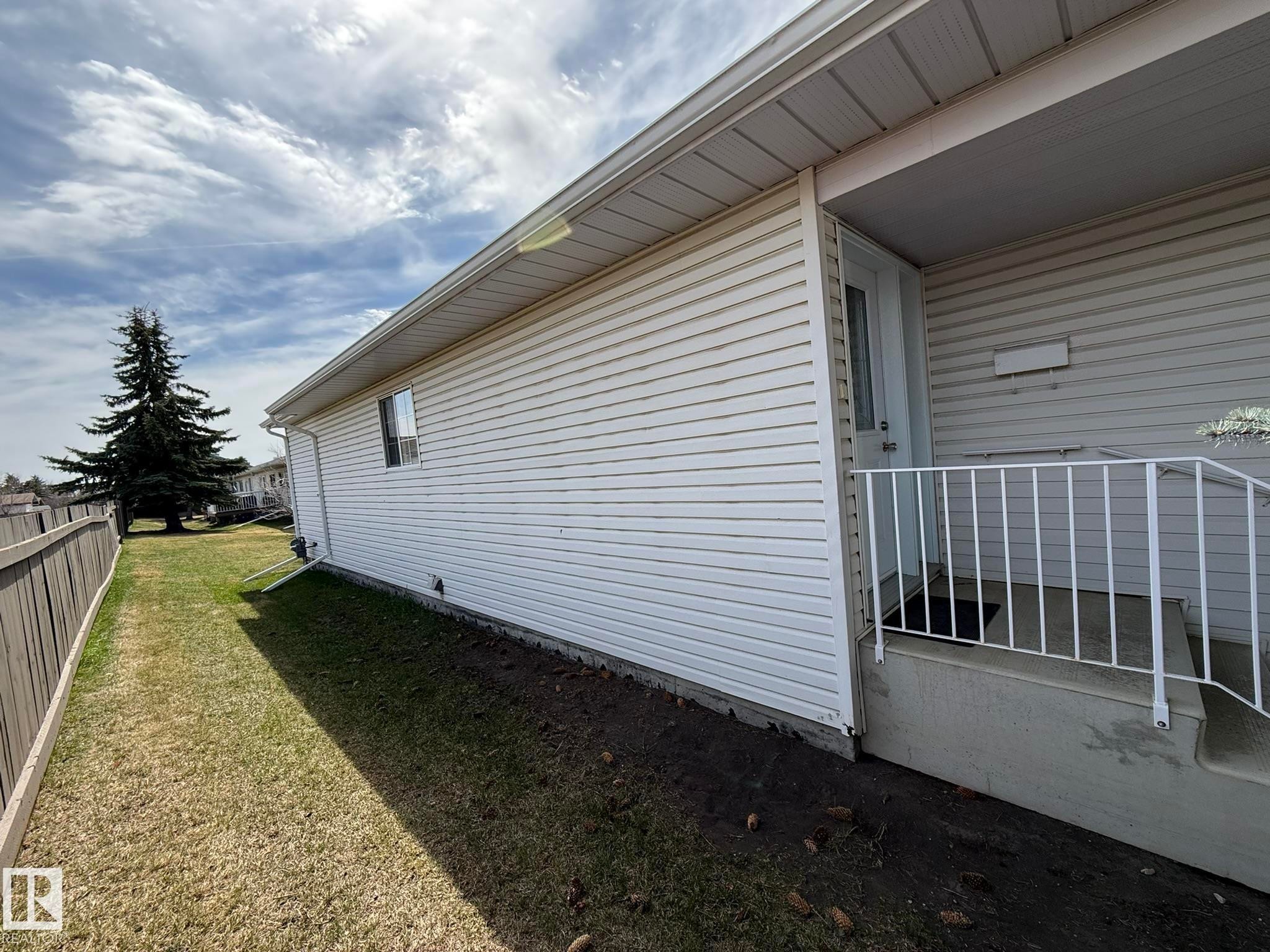 Exterior features include white vinyl siding, a covered entry with white railings, and a side yard with mature landscaping - 102 4610 50 Avenue, Stony Plain, AB