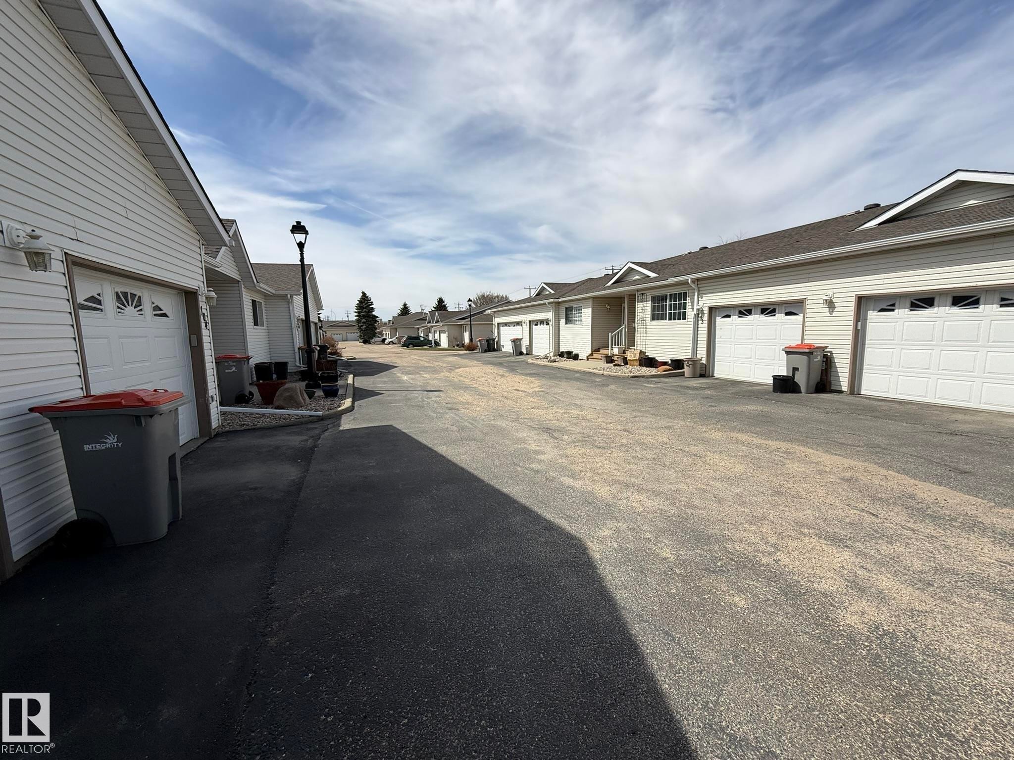 Row of residential units featuring white siding and individual attached garages - 102 4610 50 Avenue, Stony Plain, AB