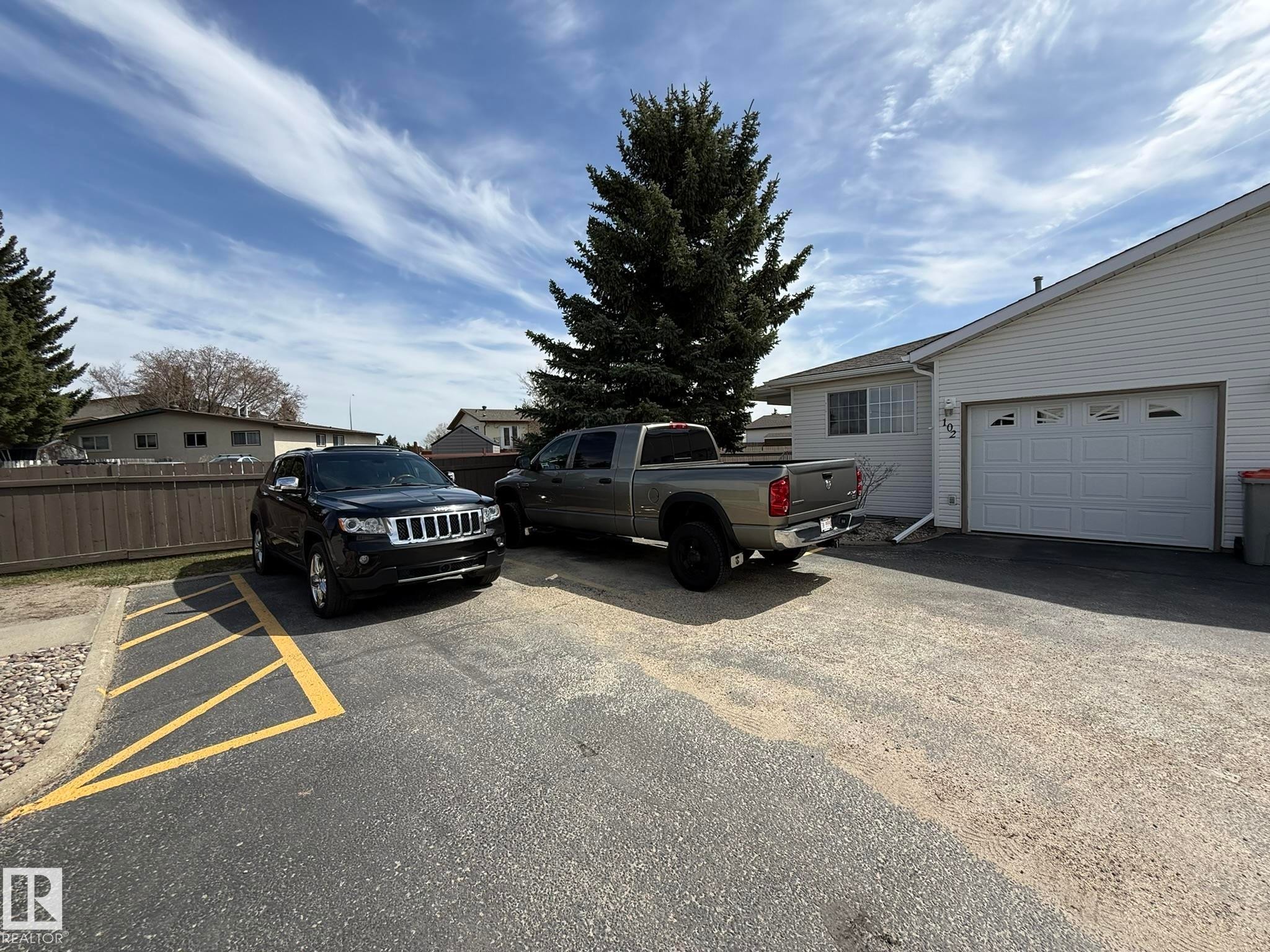 White vinyl siding exterior featuring an attached garage with a white panel door - 102 4610 50 Avenue, Stony Plain, AB