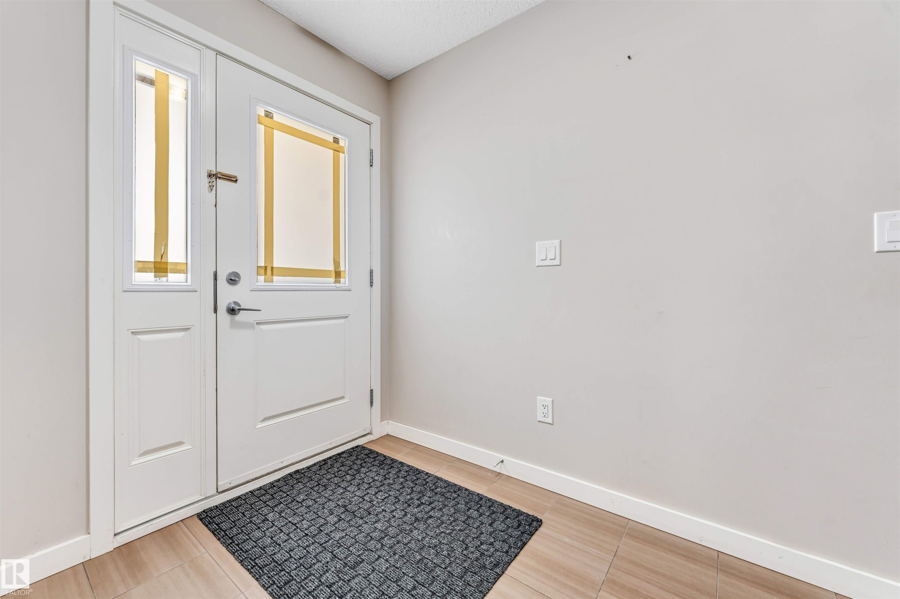Entryway featuring a white paneled front door with a transom window, a sidelight, and light-toned tile flooring - 1624 33A Street, Edmonton, AB