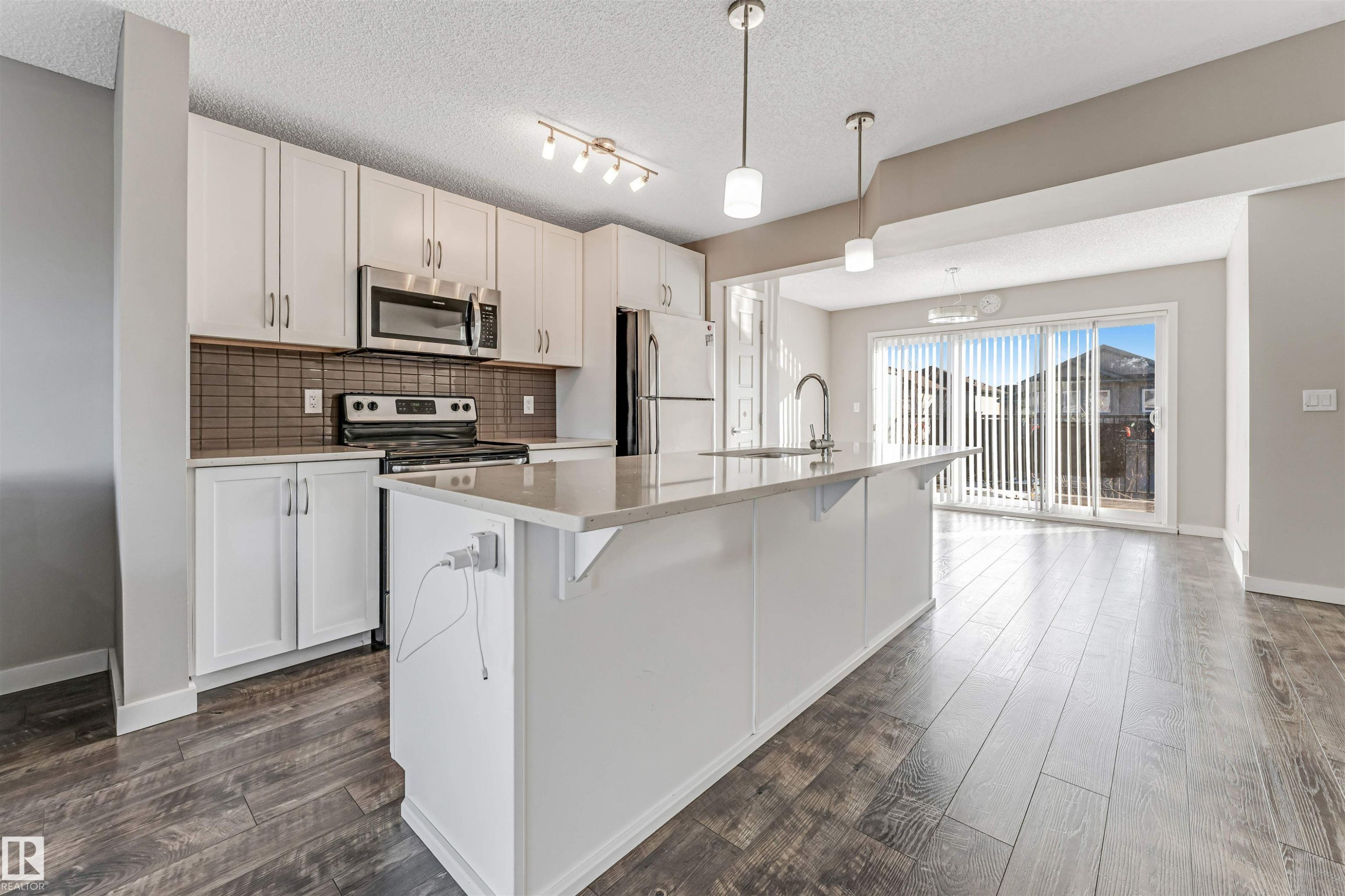 Kitchen featuring white cabinetry, stainless steel appliances, a large island with sink, dark subway tile backsplash, and wood-finish flooring - 1624 33A Street, Edmonton, AB