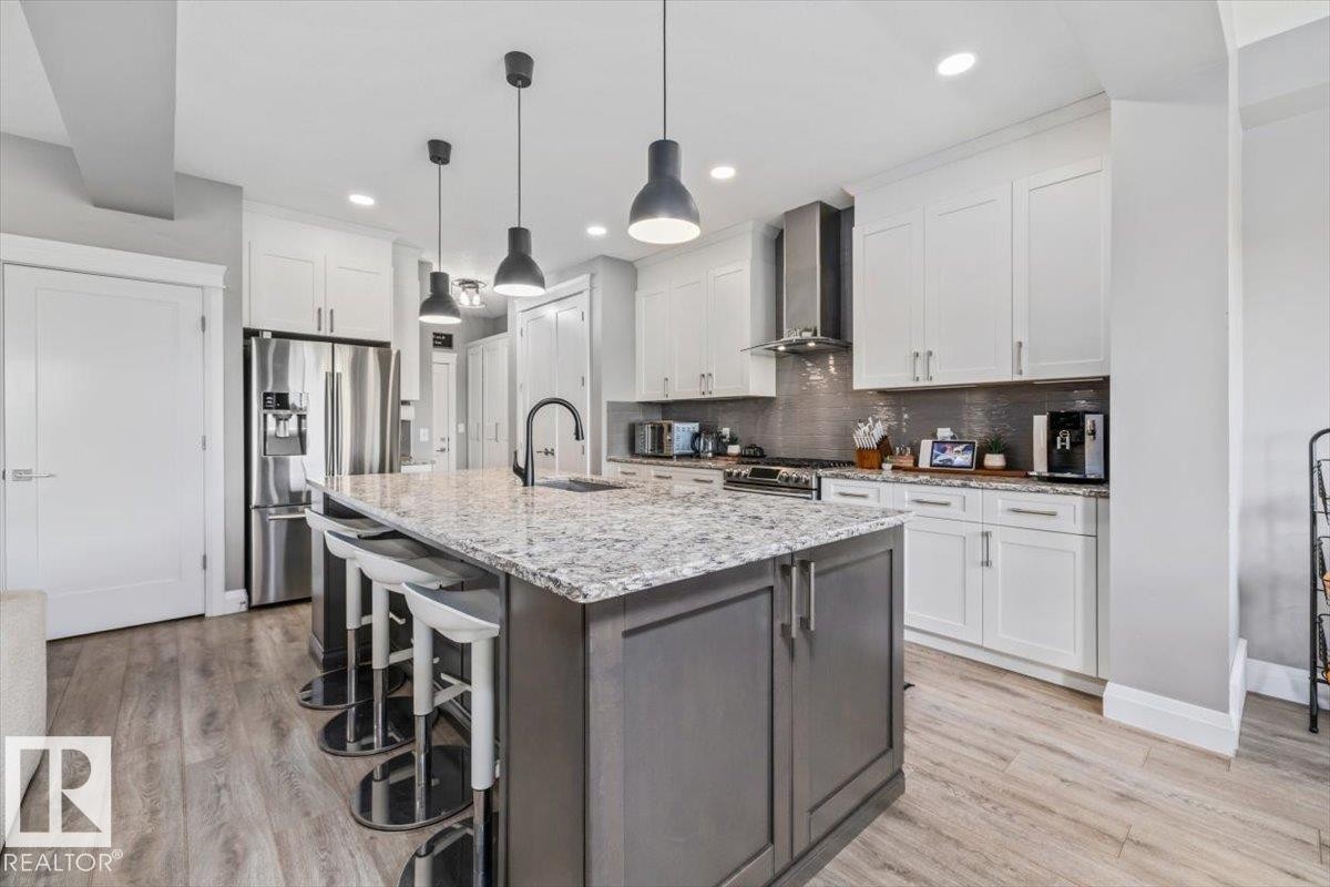 Spacious kitchen featuring a large island with a granite countertop, white upper and lower cabinetry, stainless steel appliances, and natural gas range - 54 Spring Gate, Spruce Grove, AB