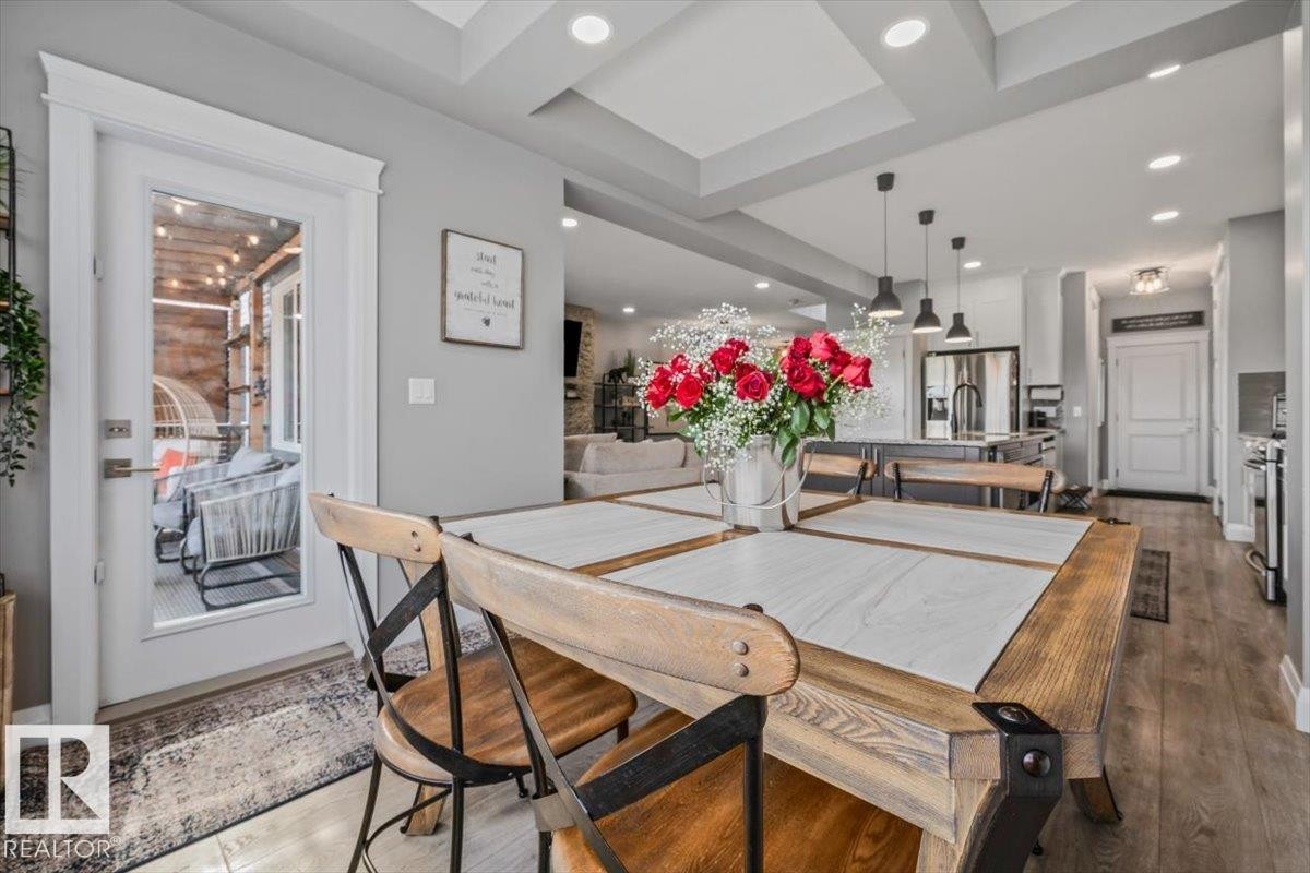 Dining area featuring a coffered ceiling with recessed lighting, LVP flooring, and a patio door leading to an outdoor living space - 54 Spring Gate, Spruce Grove, AB
