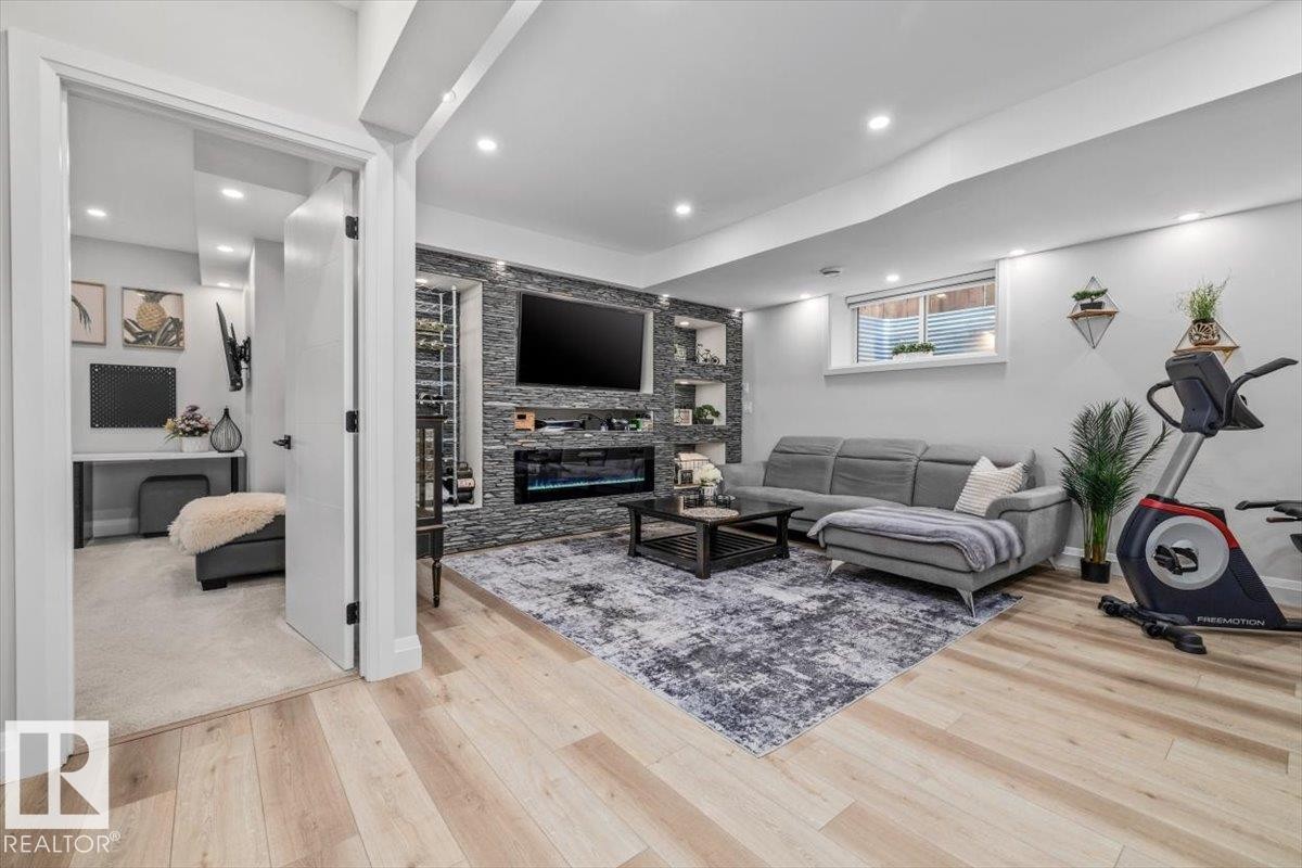 Finished lower level featuring a textured stone accent wall with an integrated electric fireplace, light wood-finish flooring and recessed lighting - 54 Spring Gate, Spruce Grove, AB