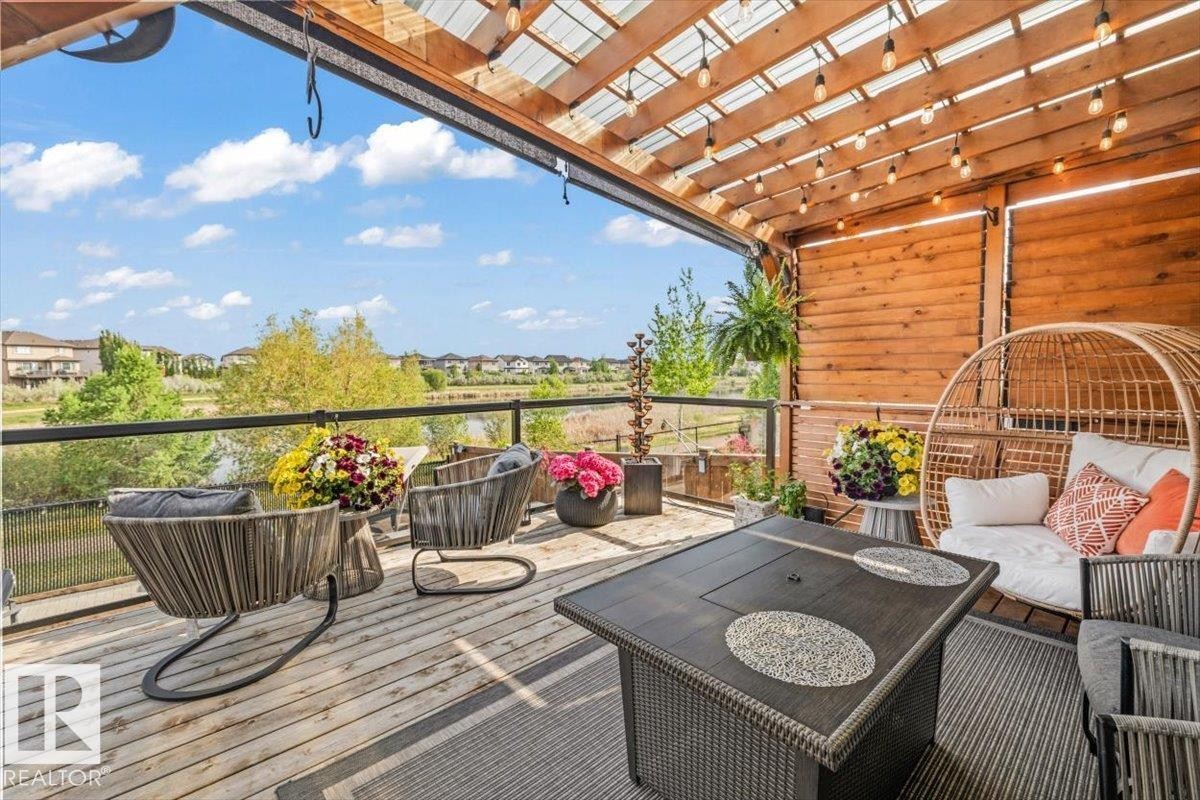 Expansive outdoor deck featuring cedar wood-decking, a clear glass railing, and a wood slat pergola - 54 Spring Gate, Spruce Grove, AB