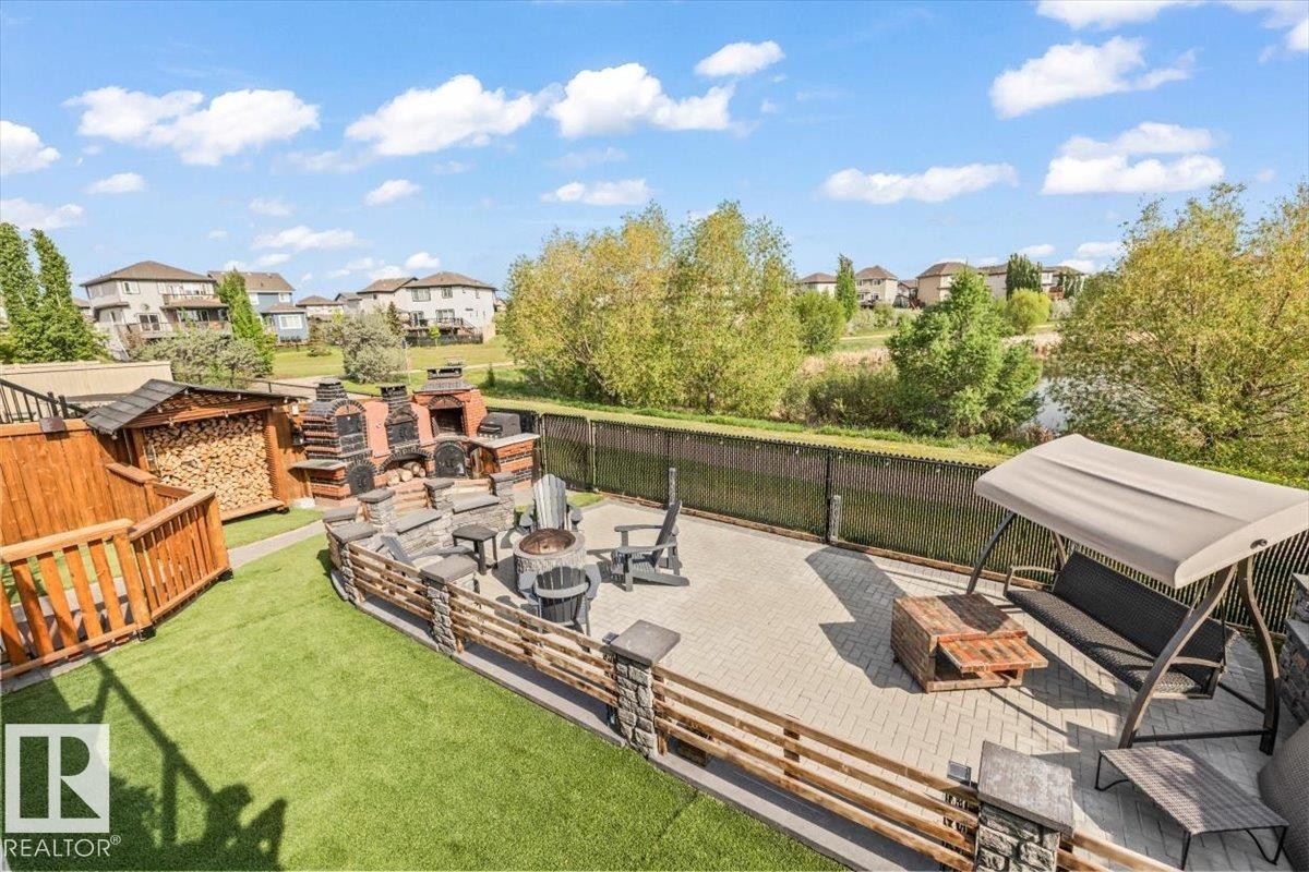 Expansive outdoor living area featuring a paver patio with a stone fire pit, a built-in masonry outdoor kitchen with smoker, pizza oven, fire & BBQ areas, and a wood storage - 54 Spring Gate, Spruce Grove, AB