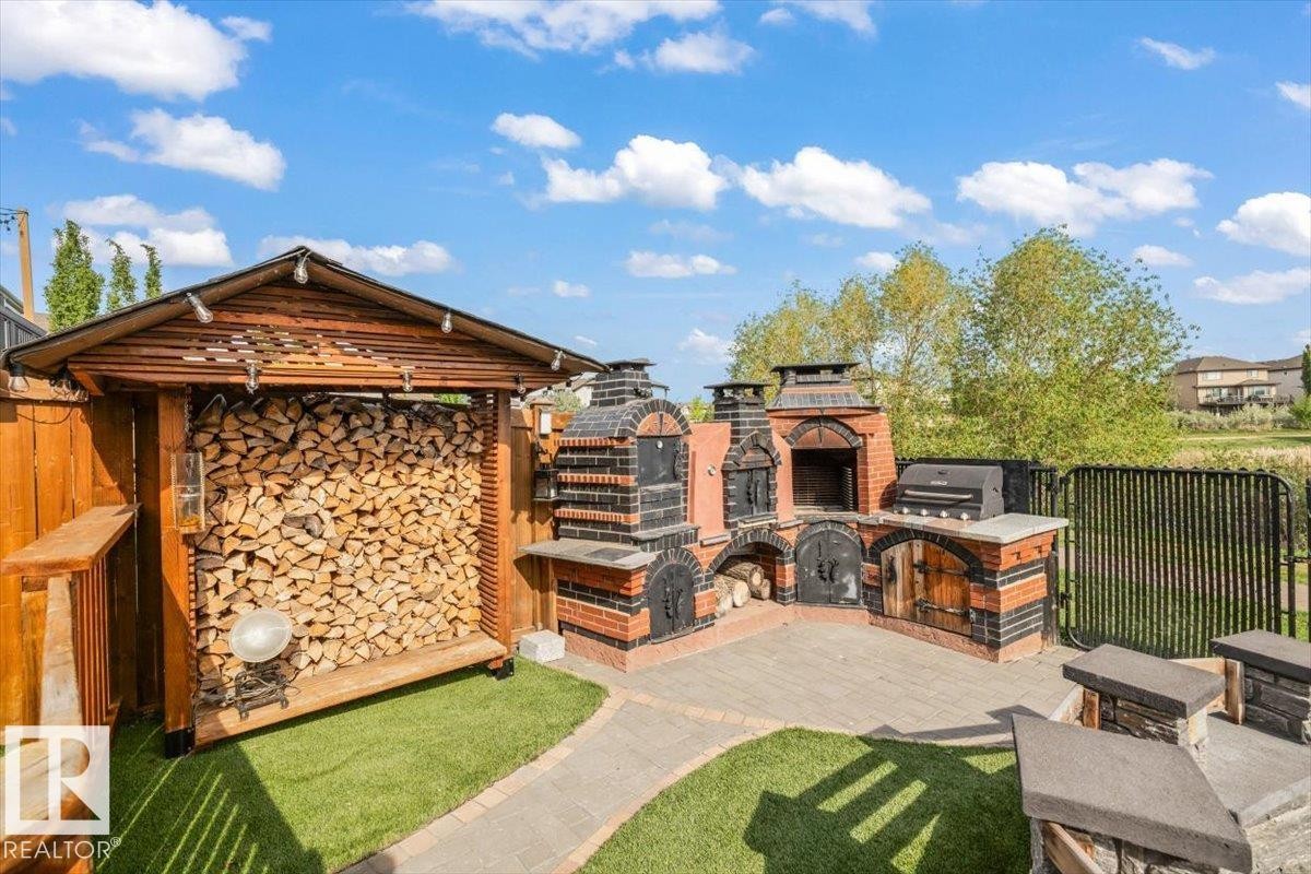 Expansive outdoor masonry kitchen featuring a brick-built pizza oven, smoker, fire pit and BBQ area - 54 Spring Gate, Spruce Grove, AB