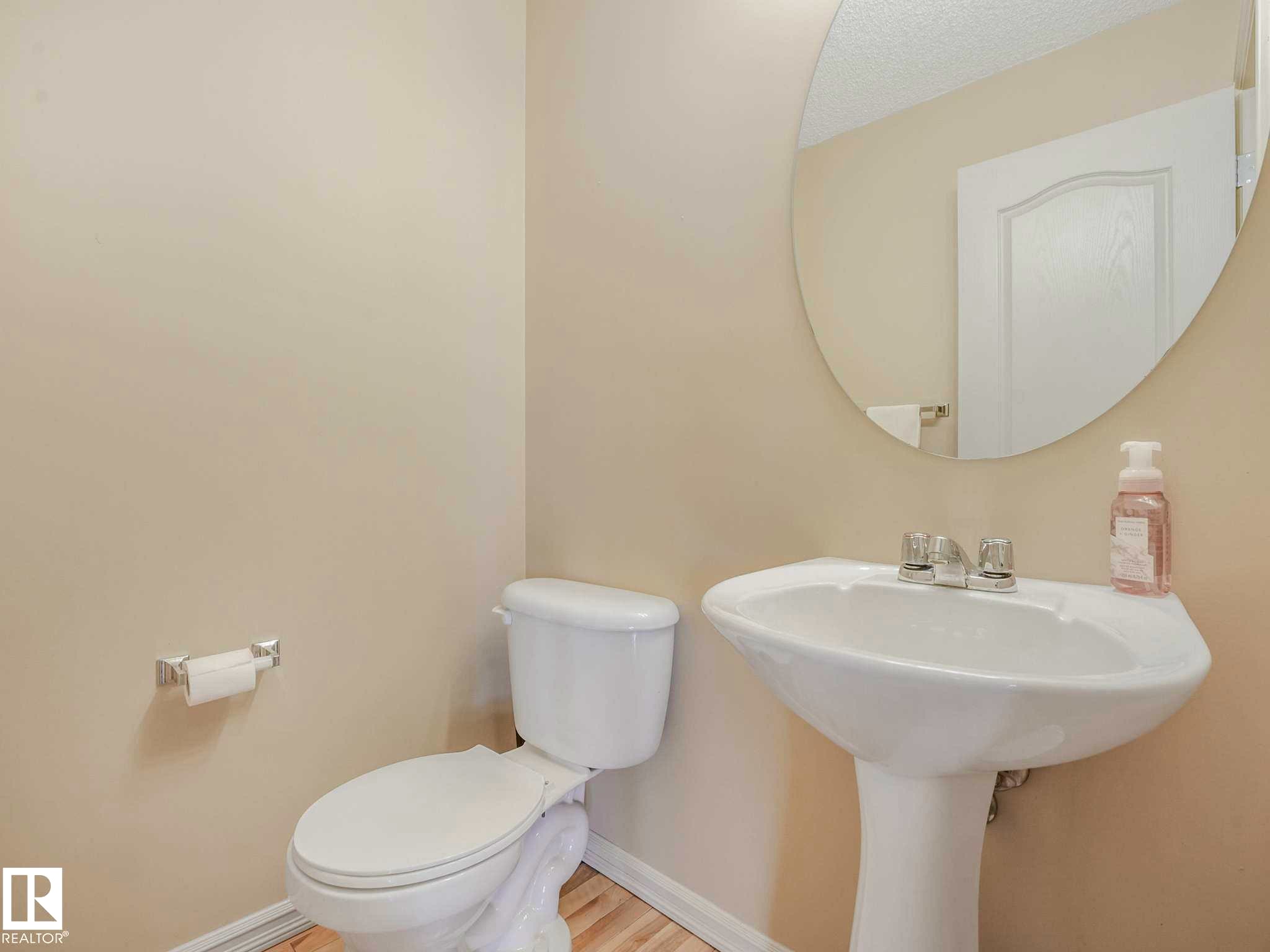 Pedestal sink with chrome fixtures, oval mirror, and light-toned flooring - 1116 Lincoln Crescent, Edmonton, AB - Indoor Photo Showing Bathroom