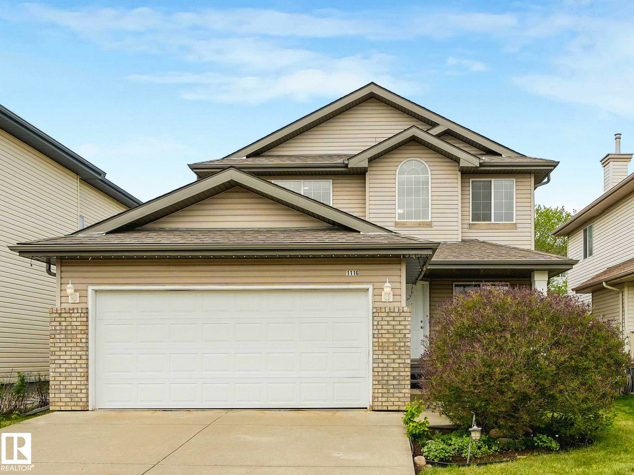 Two-story residence featuring light-toned siding, a two-car garage, brick accents, and a prominent arched window on the second level - 1116 Lincoln Crescent, Edmonton, AB - Outdoor