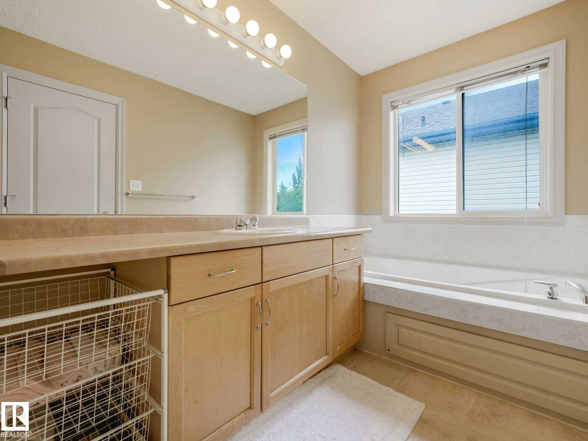 Bathroom featuring a light-toned vanity with integrated sink, a large mirror, and overhead strip lighting - 1116 Lincoln Crescent, Edmonton, AB - Indoor Photo Showing Bathroom
