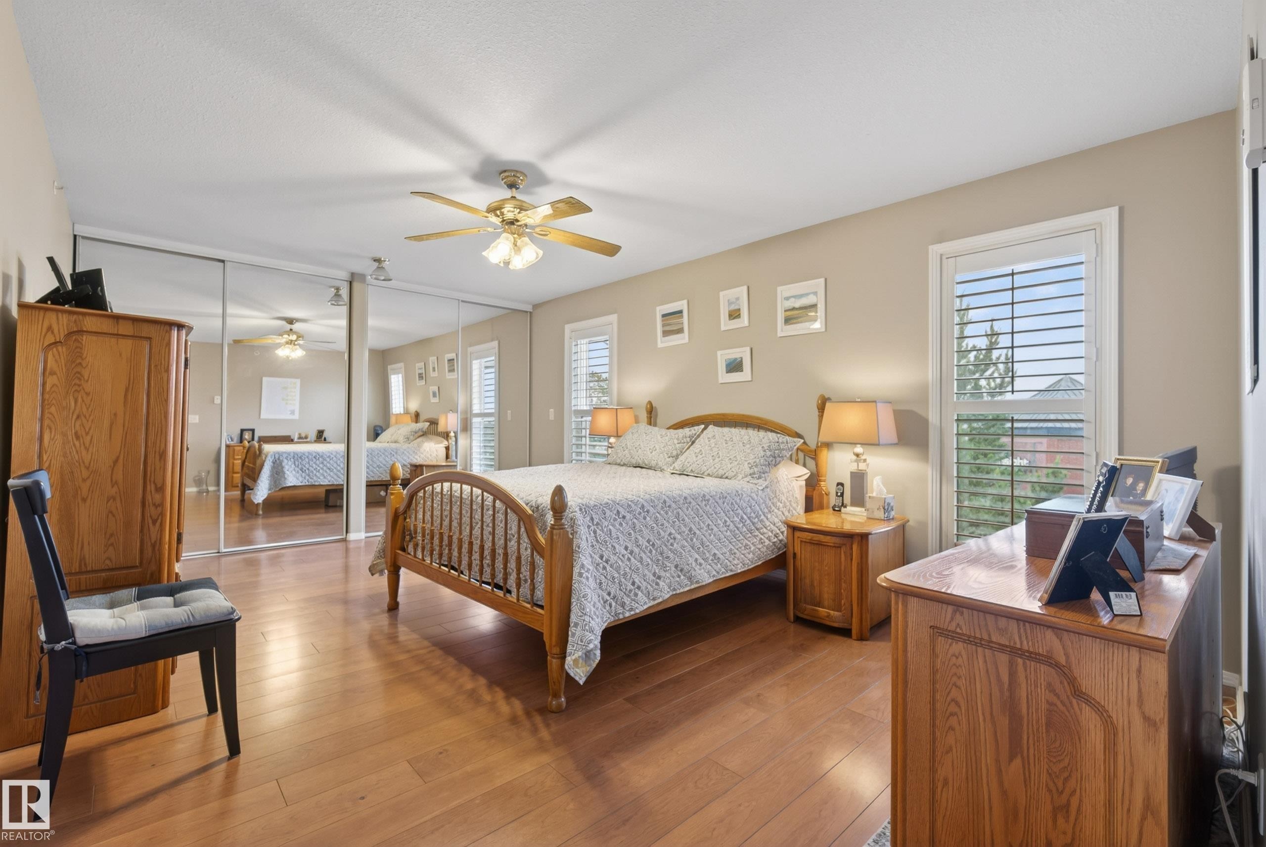 Bedroom featuring wood-finish flooring, mirrored closet doors, and a ceiling fan - 413 8912 156 Street Nw, Edmonton, AB
