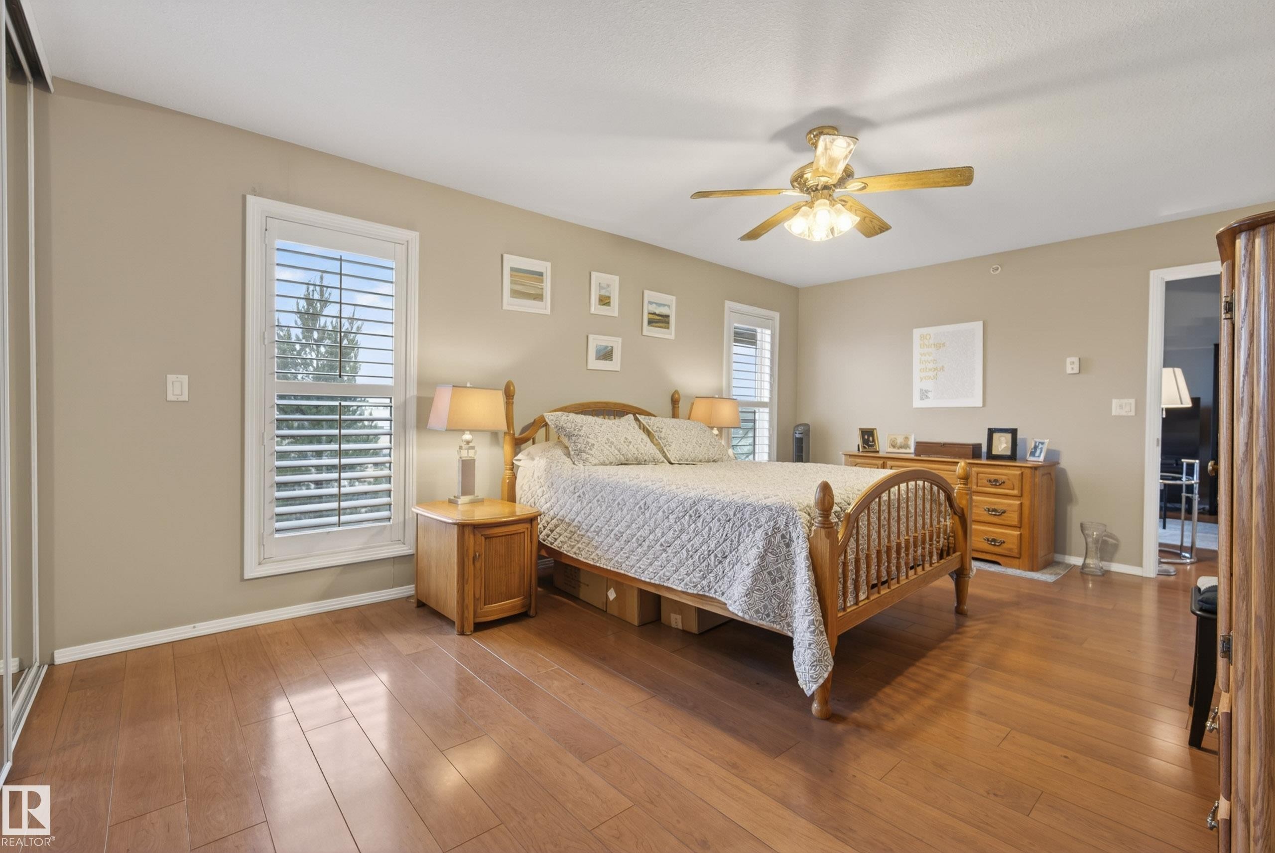 Spacious room featuring wood-finish flooring, neutral-toned walls, and white plantation shutters on windows - 413 8912 156 Street Nw, Edmonton, AB