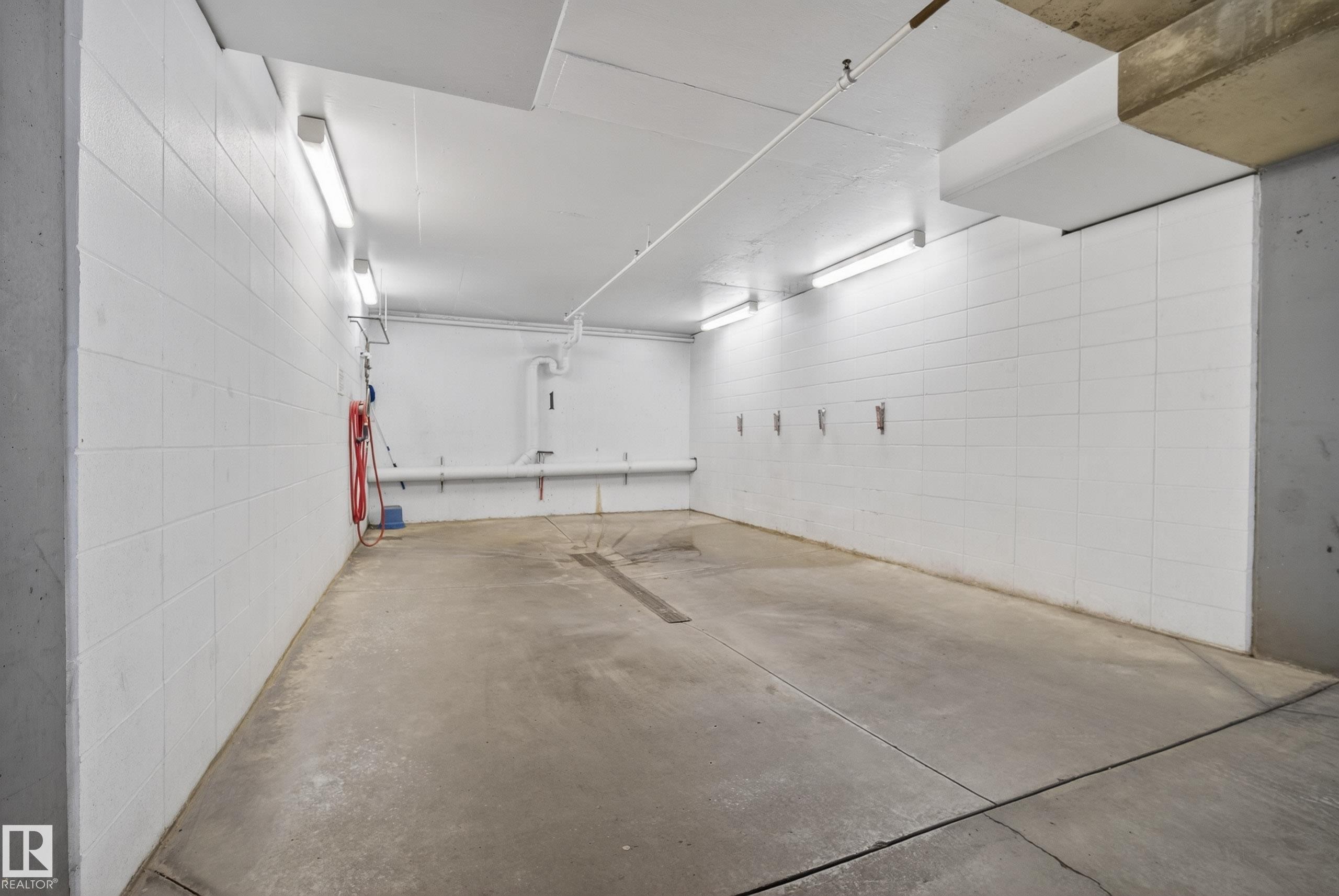 Concrete flooring with drainage channel, white block walls, and overhead fluorescent lighting - 413 8912 156 Street Nw, Edmonton, AB