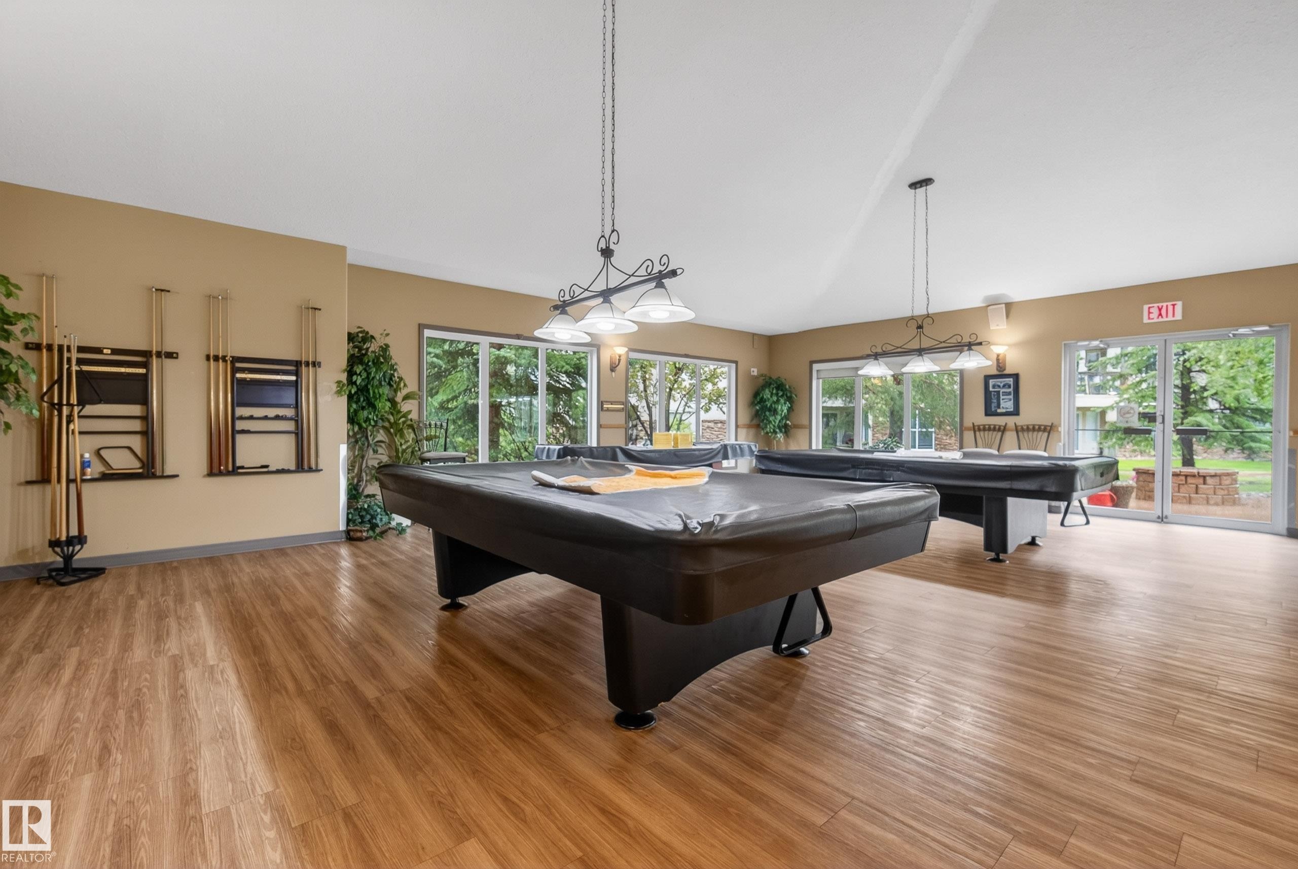 Spacious recreation room featuring two billiard tables, wood-finish flooring, and multiple glass sliding doors providing exterior access - 413 8912 156 Street Nw, Edmonton, AB