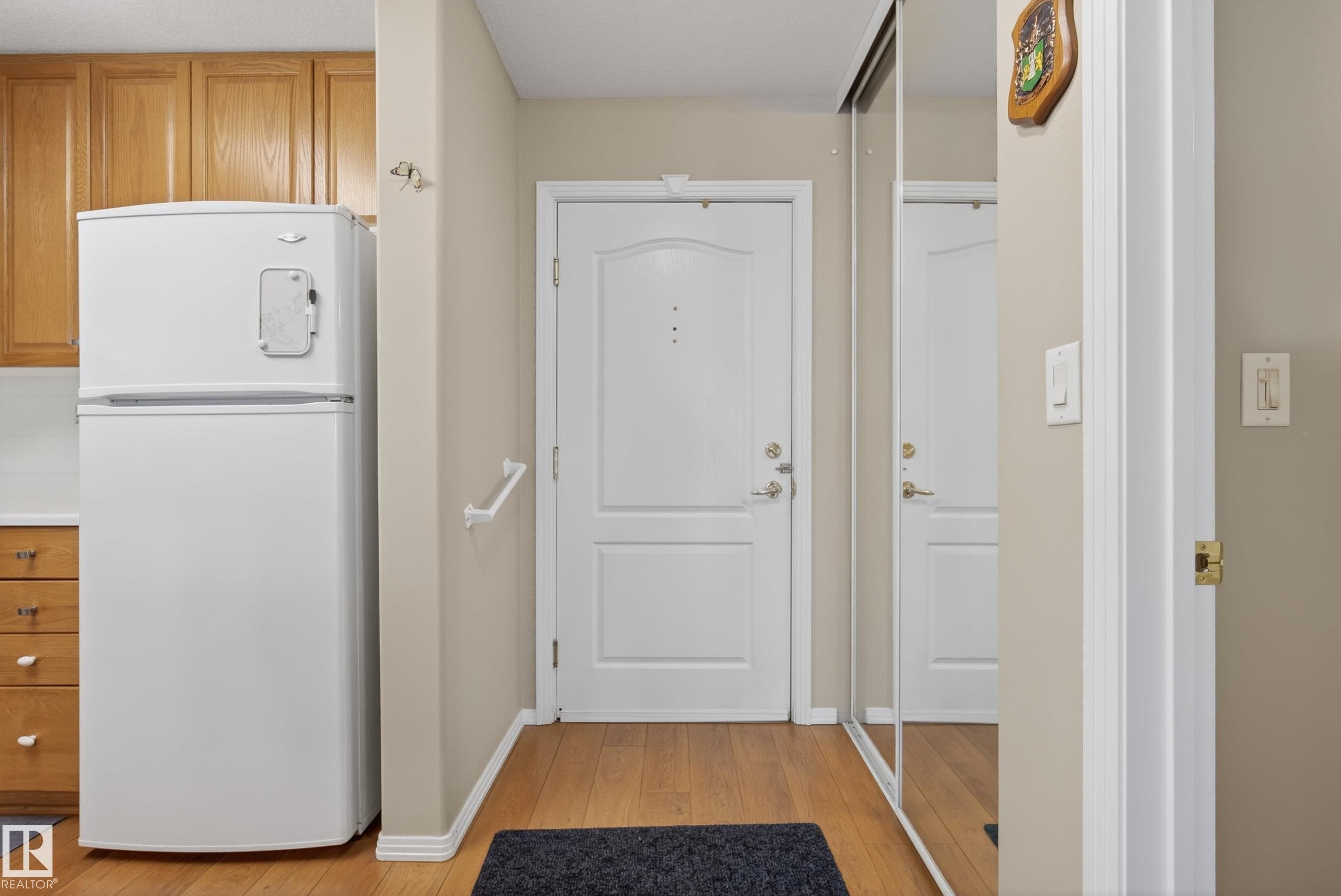 Entryway featuring wood-finish flooring, a white paneled door, and mirrored closet doors - 413 8912 156 Street Nw, Edmonton, AB
