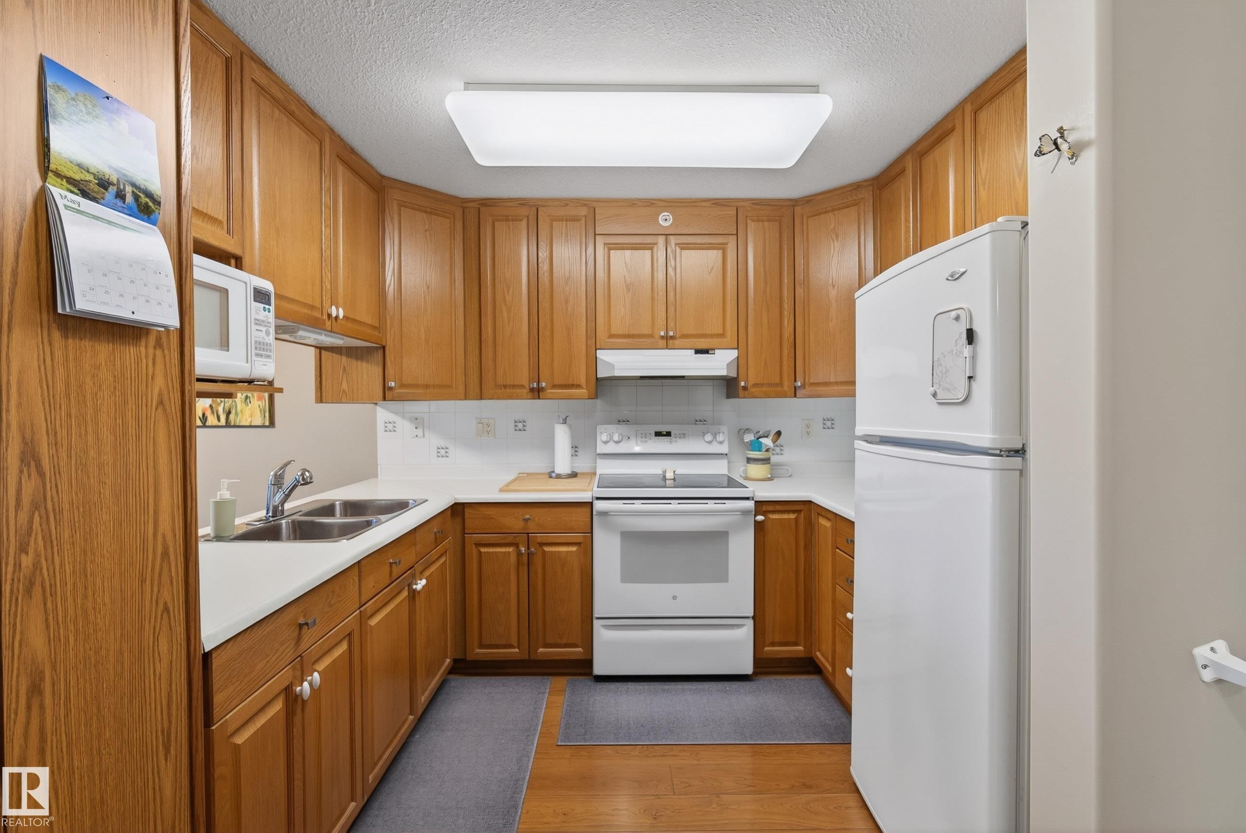 Full kitchen featuring wood-finish cabinetry, white countertops, and a white tile backsplash - 413 8912 156 Street Nw, Edmonton, AB