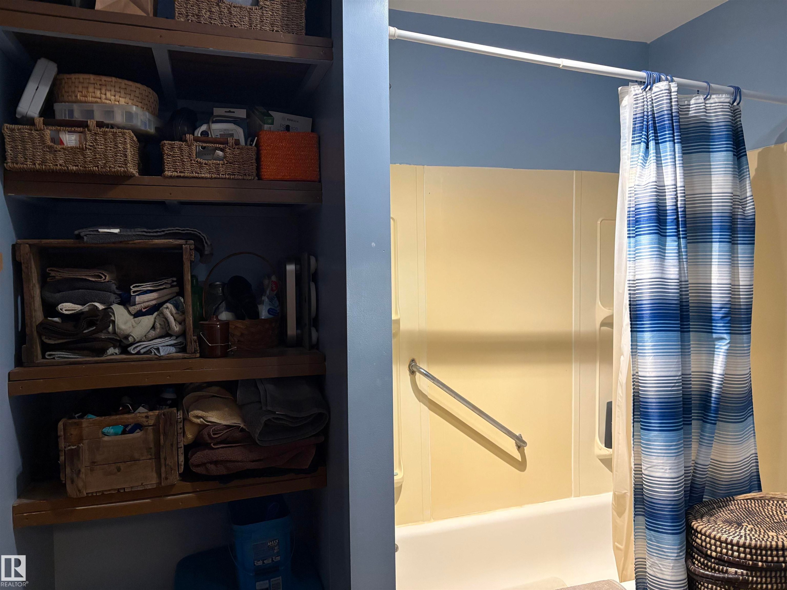 Bathroom featuring a built-in tub with a grab bar, a shower surround, and integrated shelving. - 125 56524 Rng Rd 52A, Lindbergh, AB