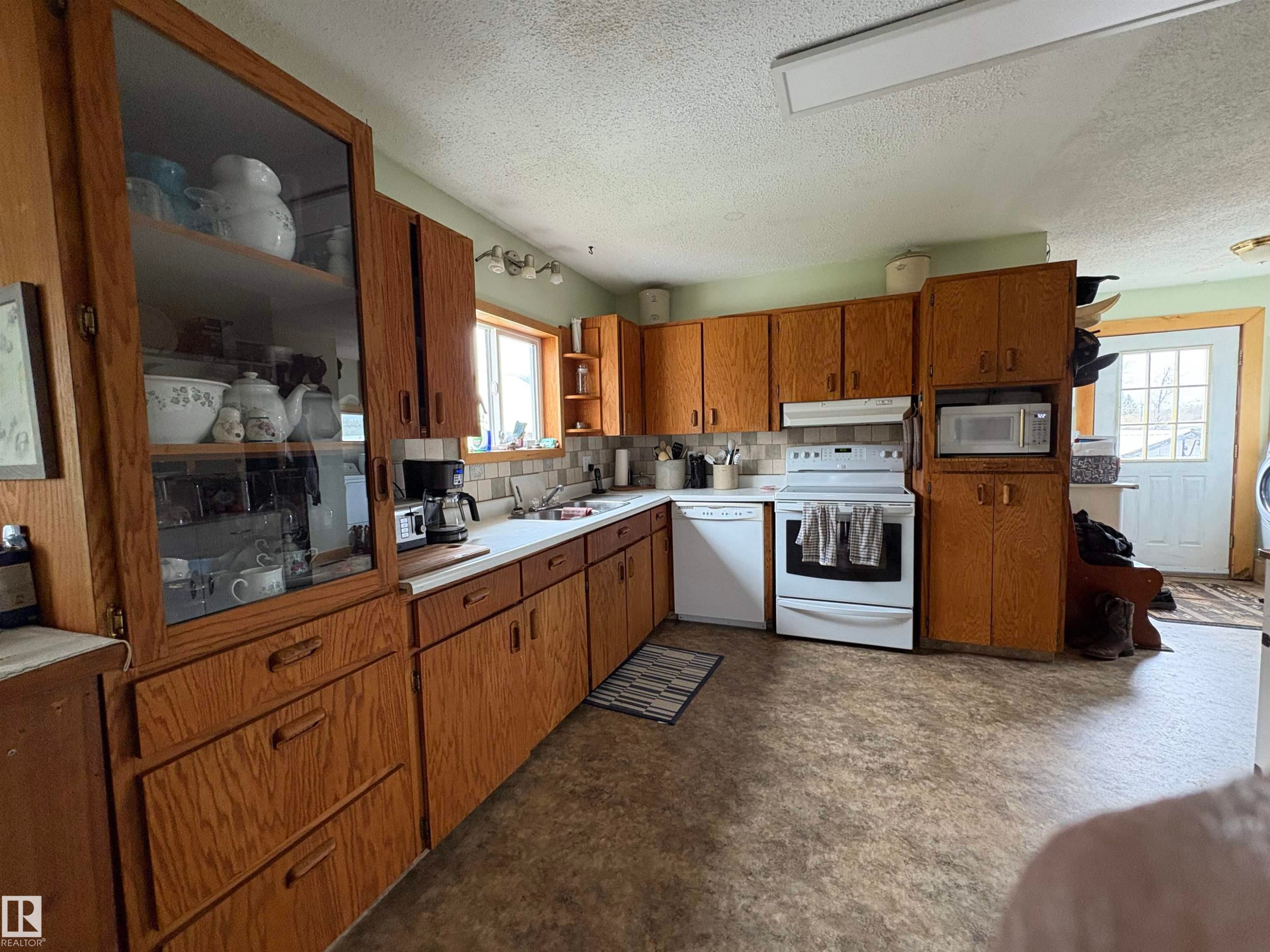 Kitchen featuring wood cabinetry, white appliances, a light-toned countertop, and a tiled backsplash. - 125 56524 Rng Rd 52A, Lindbergh, AB