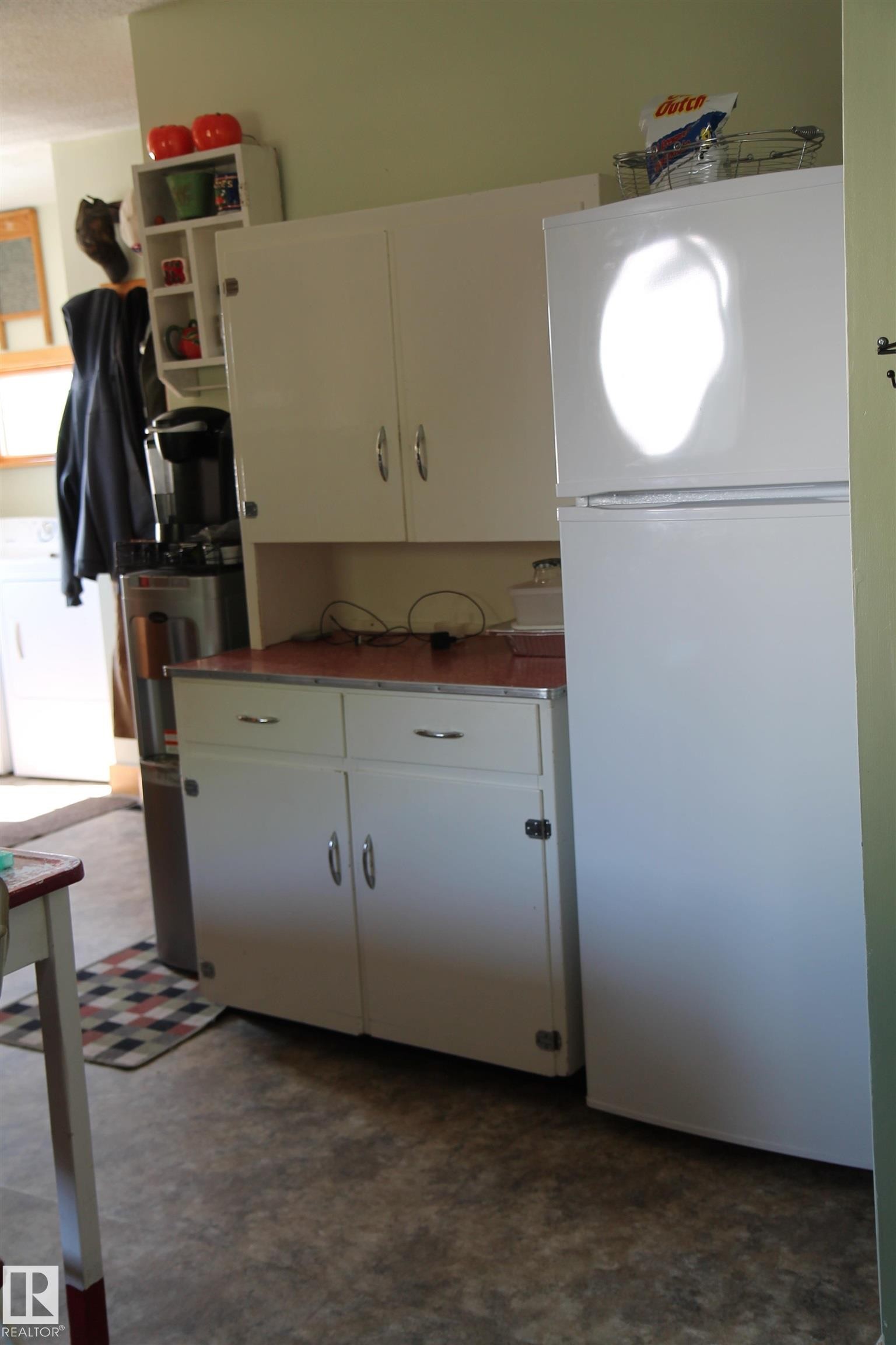Kitchen area featuring white cabinetry with brushed nickel hardware, a white top-freezer refrigerator, and a speckled resilient flooring. - 125 56524 Rng Rd 52A, Lindbergh, AB