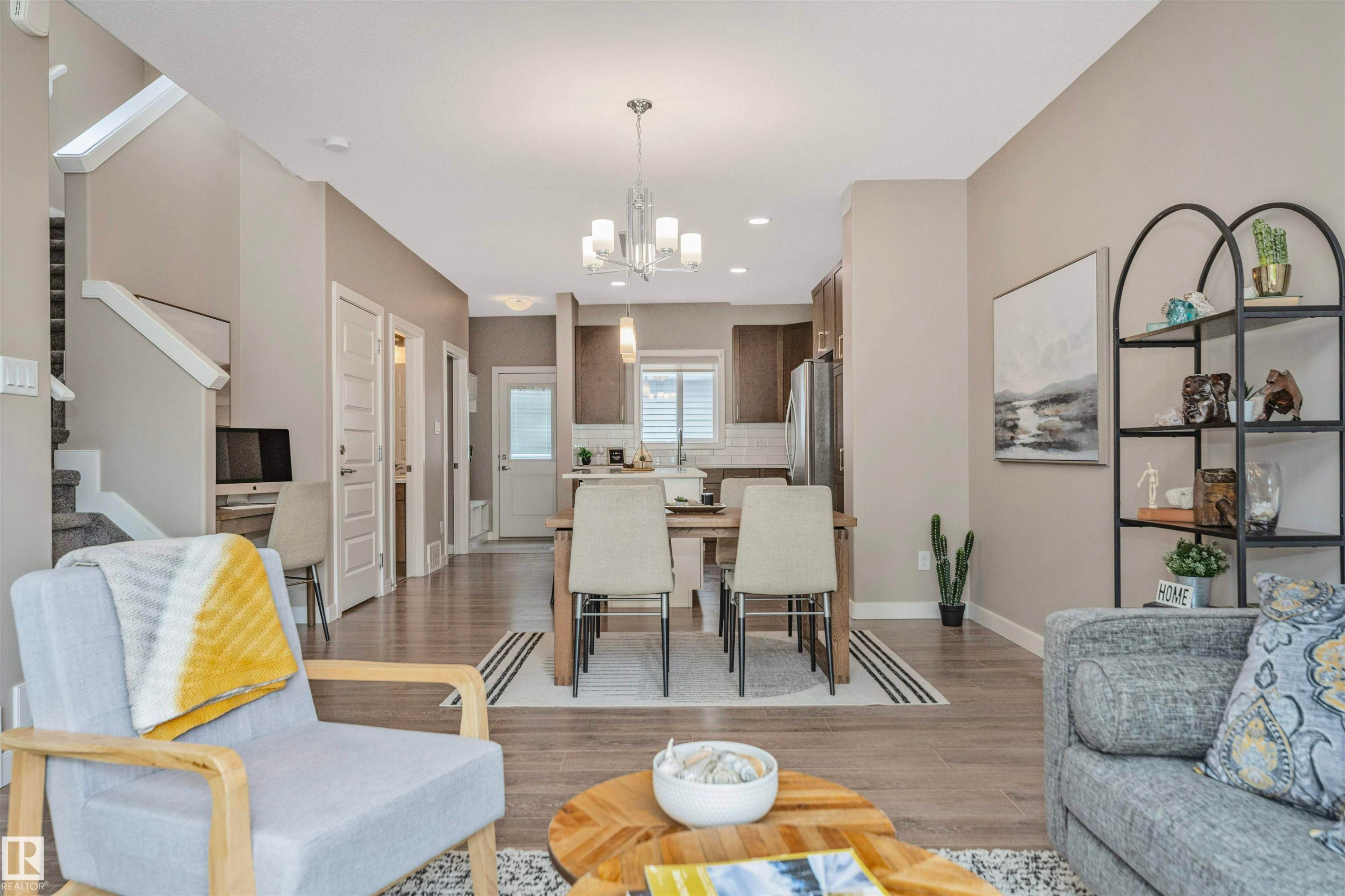 Open-concept living area featuring wood-finish flooring throughout, leading to a dining space with a chandelier and a kitchen beyond - 22124 85 Avenue Nw, Edmonton, AB - Indoor Photo Showing Living Room