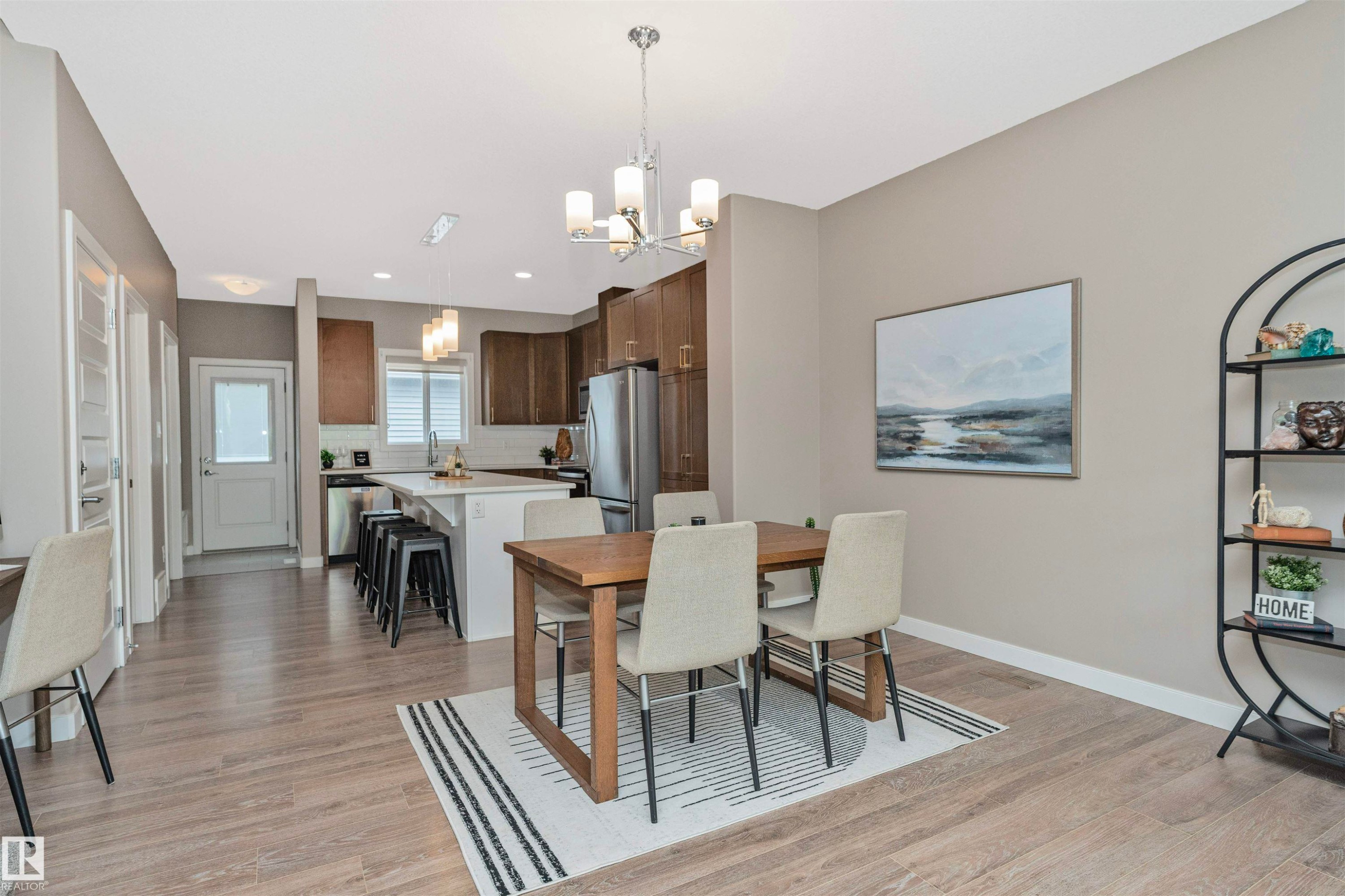 Open-concept living area featuring wood-finish flooring, a kitchen island with seating, stainless steel appliances, white subway tile backsplash, and a modern chandelier - 22124 85 Avenue Nw, Edmonton, AB - Indoor