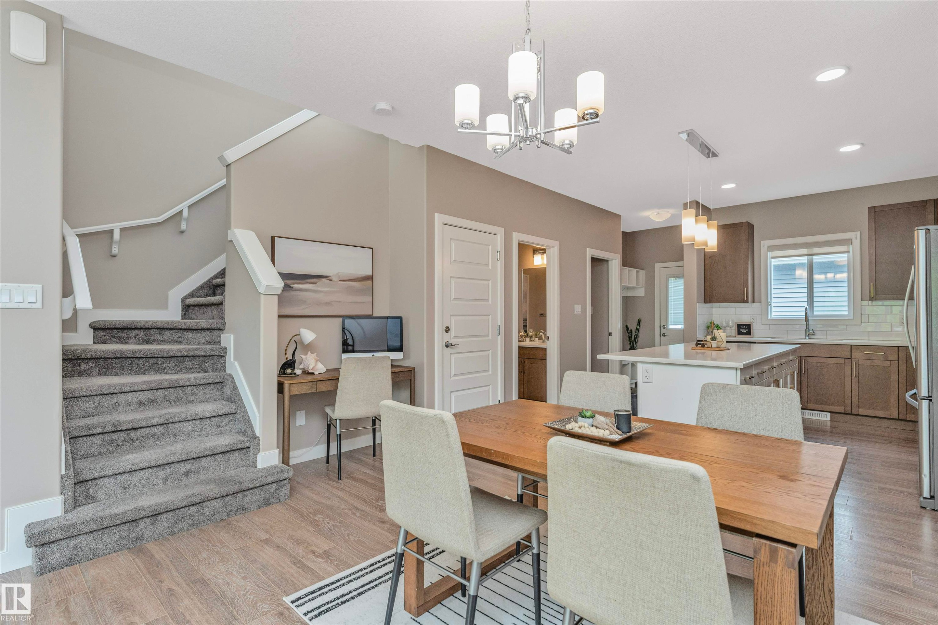 Open-concept living area featuring wood-finish flooring, a carpeted staircase with white railings, and a dining area with a modern chandelier - 22124 85 Avenue Nw, Edmonton, AB - Indoor Photo Showing Dining Room