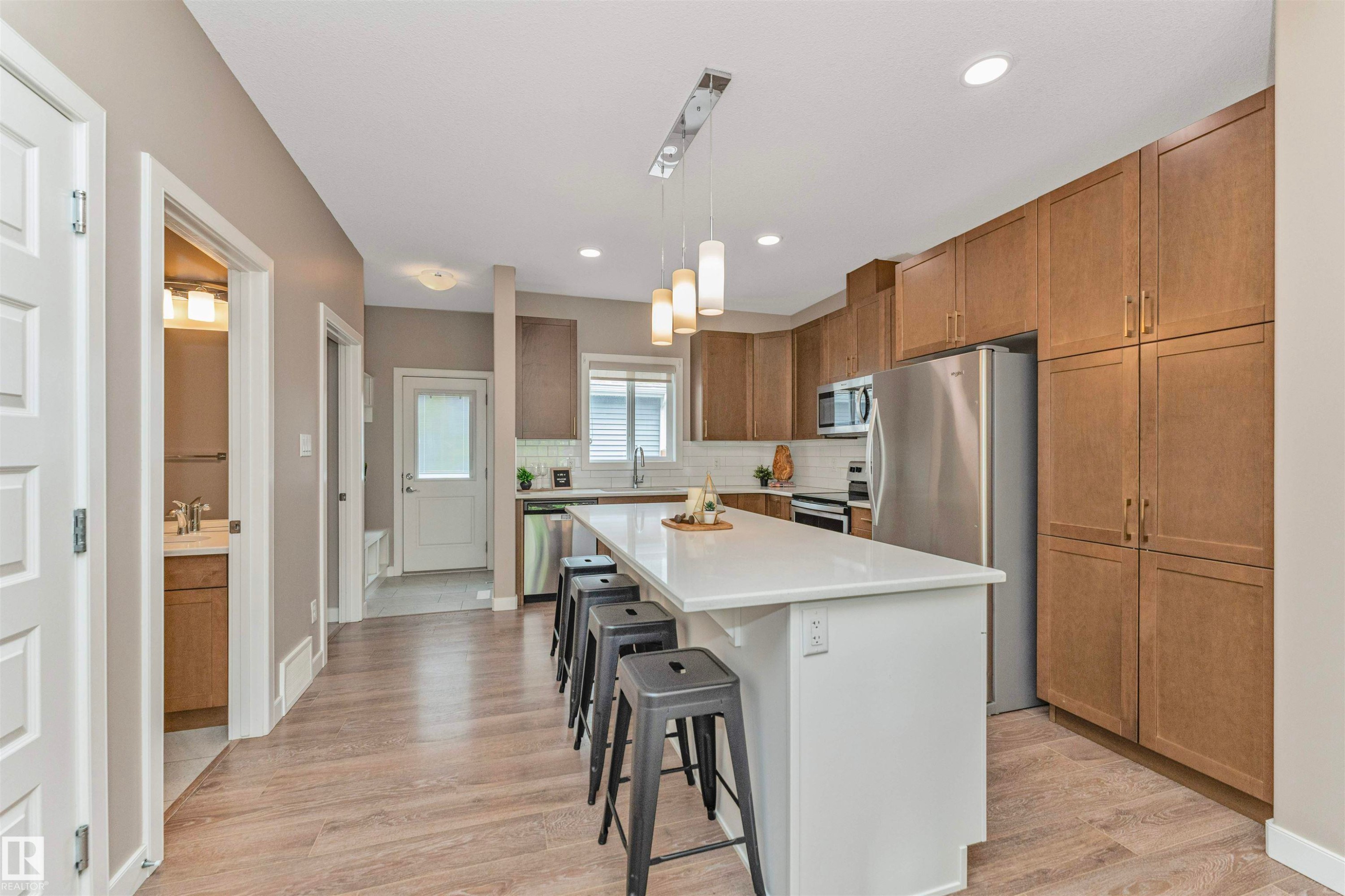 Open-concept kitchen featuring wood-finish flooring, a central island with a white countertop, and stainless steel appliances - 22124 85 Avenue Nw, Edmonton, AB - Indoor Photo Showing Kitchen With Stainless Steel Kitchen With Upgraded Kitchen