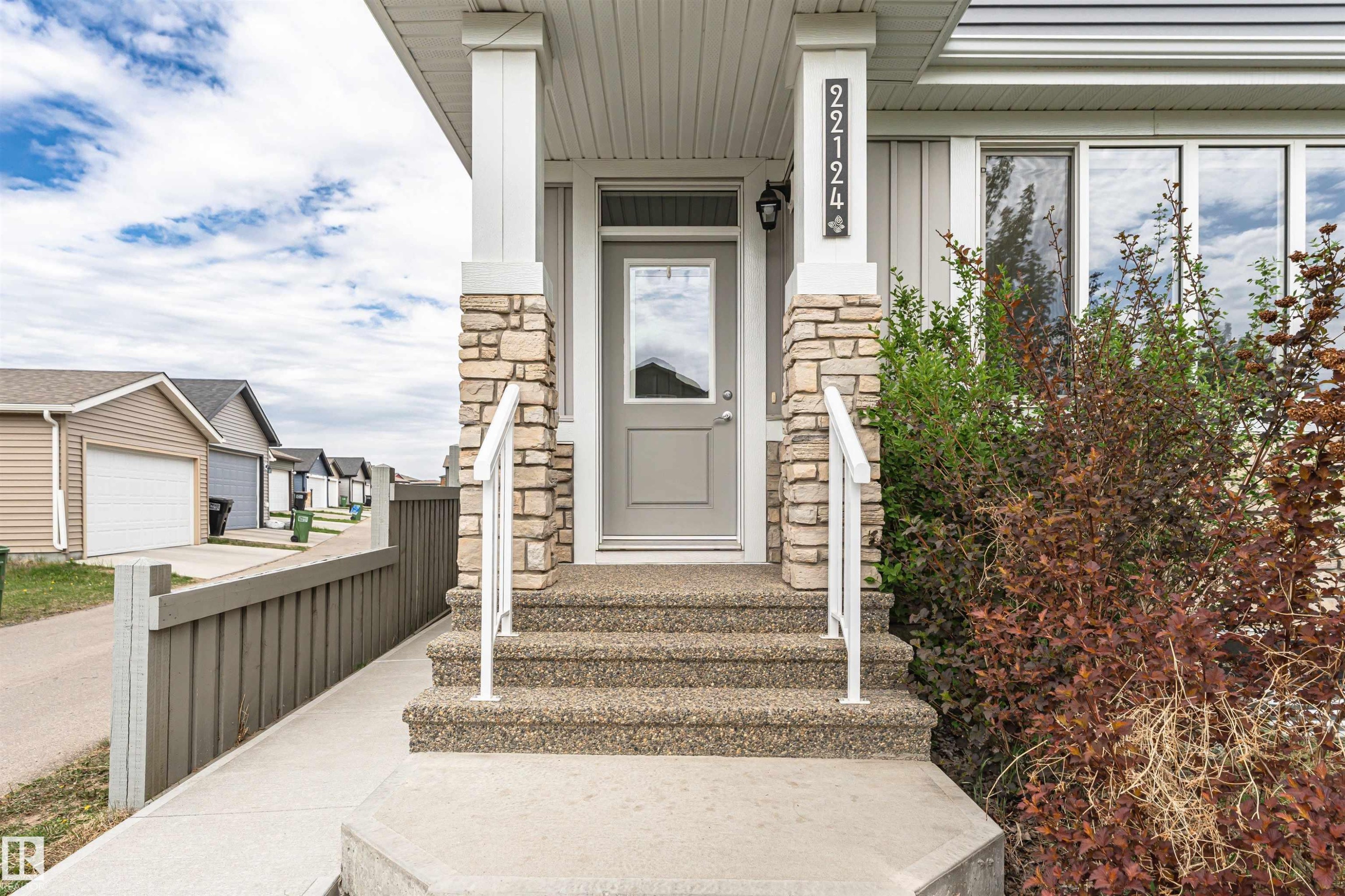 Front entrance featuring stone veneer columns, exposed aggregate steps, a full-lite entry door, and a white handrail - 22124 85 Avenue Nw, Edmonton, AB - Outdoor