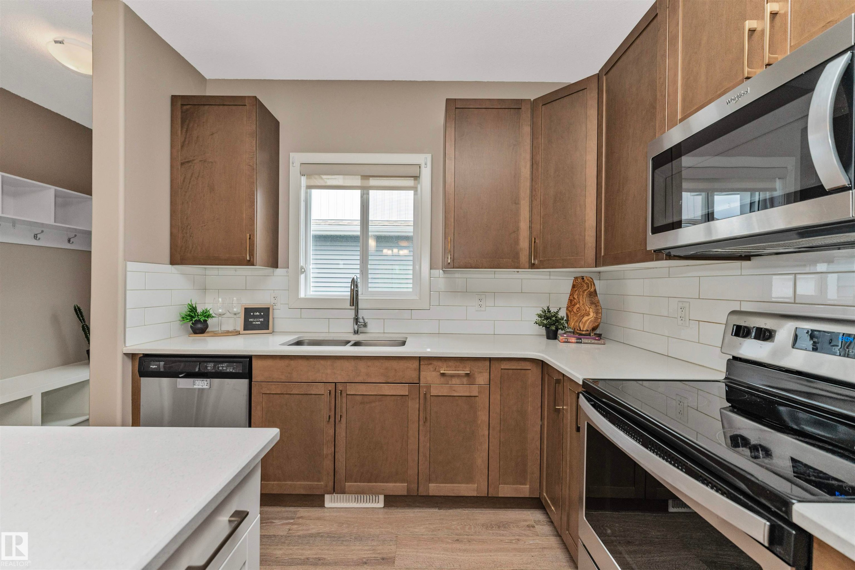 Kitchen featuring wood-finish cabinetry, white countertops, subway tile backsplash, and stainless steel appliances including a dishwasher, microwave, and electric range - 22124 85 Avenue Nw, Edmonton, AB - Indoor Photo Showing Kitchen With Stainless Steel Kitchen With Double Sink