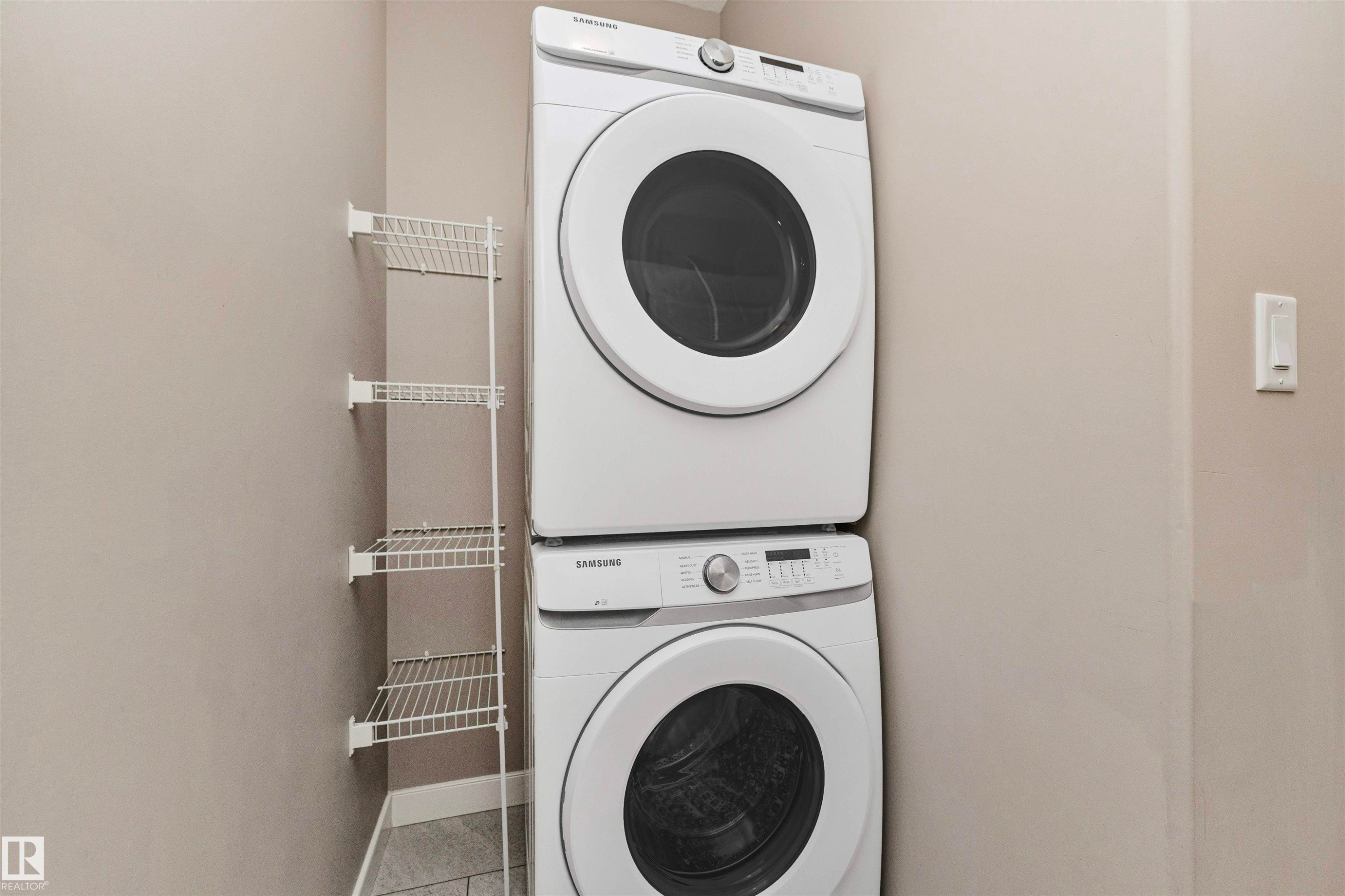 Dedicated laundry area featuring a stacked front-load washer and dryer, adjacent wall-mounted wire shelving, and light gray wall paint - 22124 85 Avenue Nw, Edmonton, AB - Indoor Photo Showing Laundry Room