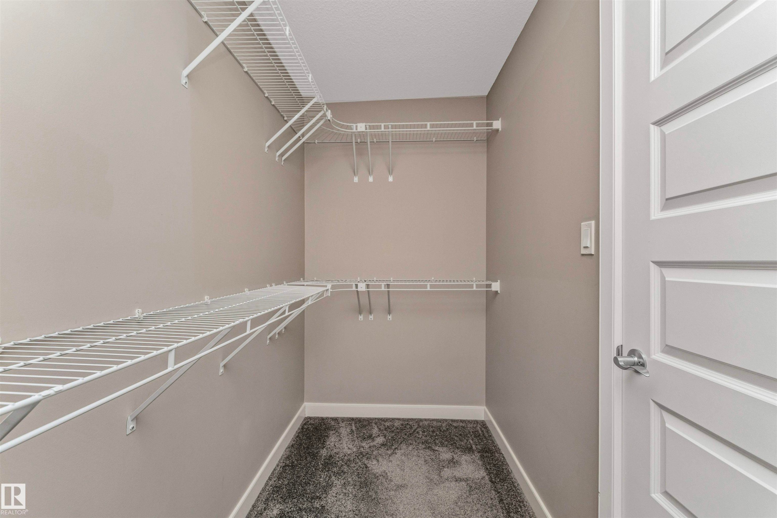 Walk-in closet with multi-level wire shelving, wire hanging rods, neutral wall paint, gray textured carpeting, and white baseboards - 22124 85 Avenue Nw, Edmonton, AB - Indoor With Storage