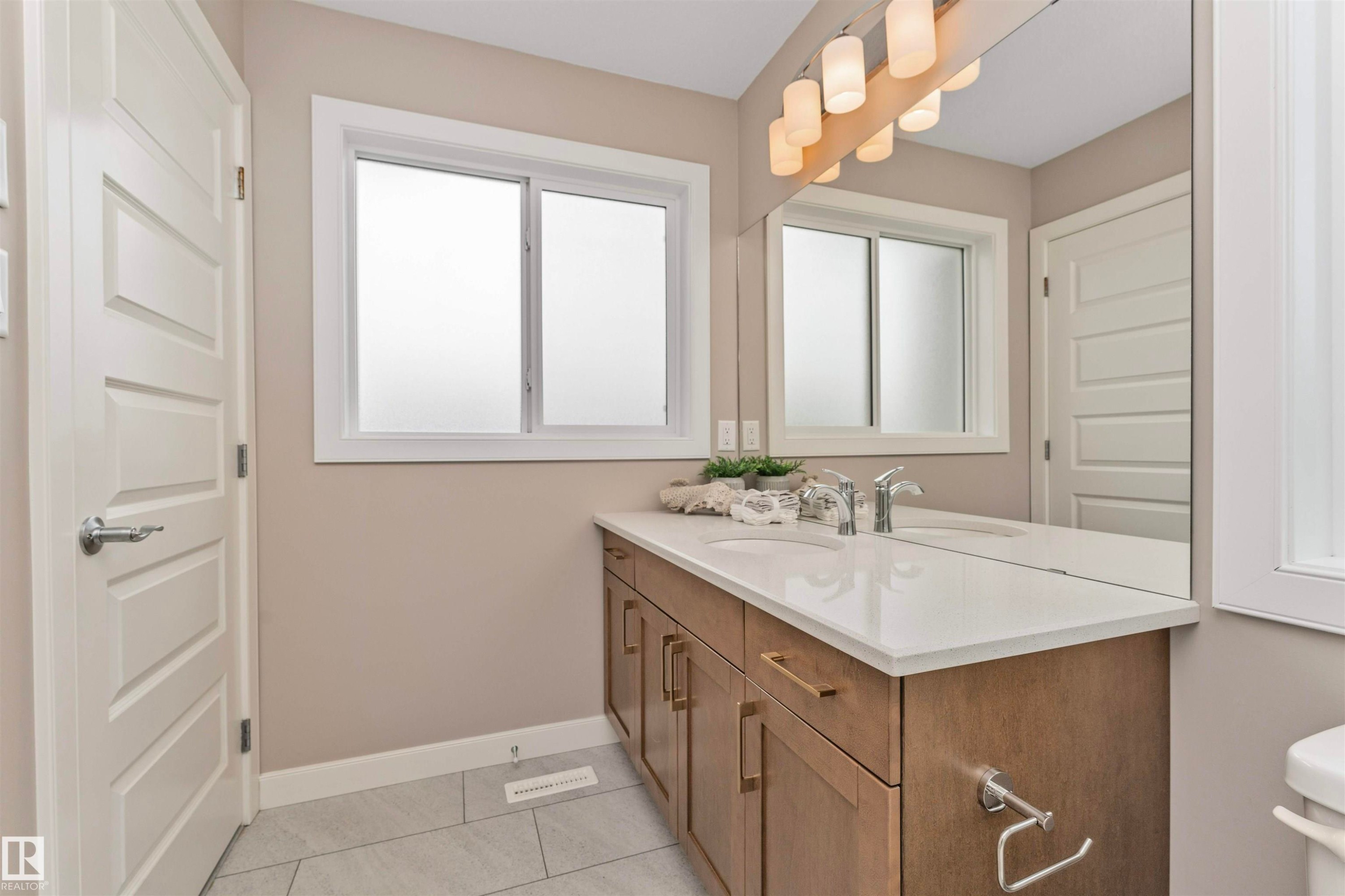 Bathroom featuring a wood-finish double vanity with white countertops, dual undermount sinks, and polished chrome faucets - 22124 85 Avenue Nw, Edmonton, AB - Indoor Photo Showing Bathroom