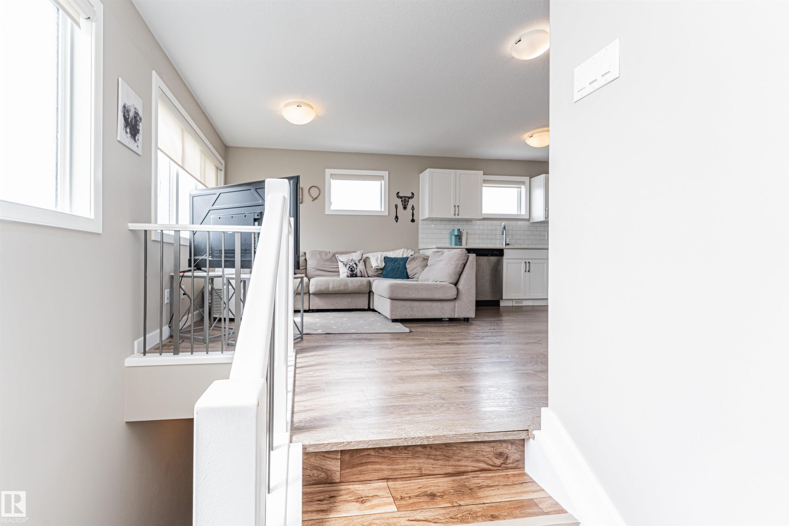 Open-concept living space featuring wood-finish flooring, white cabinetry, a stainless steel dishwasher, and recessed lighting - 22124 85 Avenue Nw, Edmonton, AB - Indoor