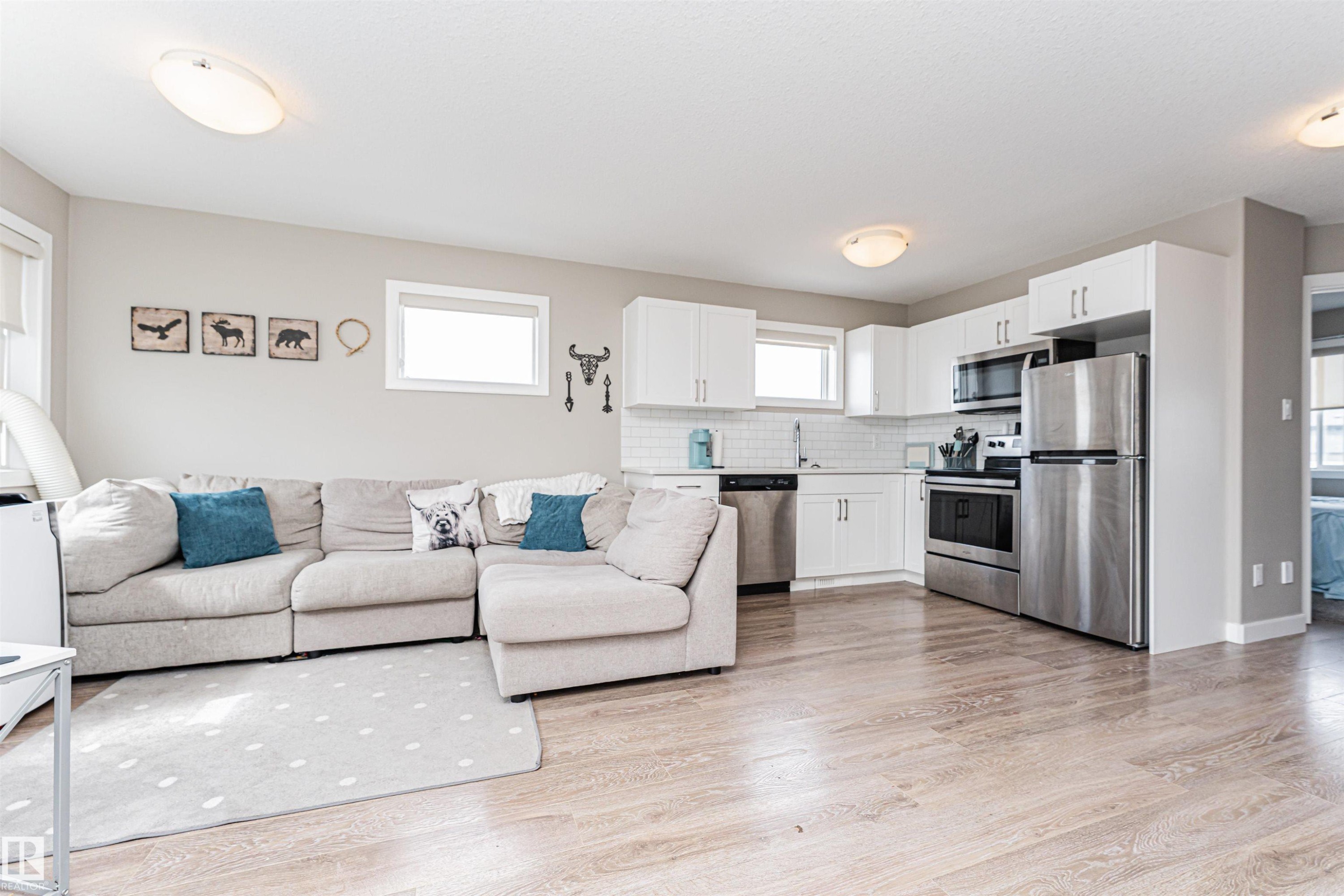 Open-concept living area featuring wood-finish flooring, white kitchen cabinetry, stainless steel appliances, a white subway tile backsplash, and recessed windows - 22124 85 Avenue Nw, Edmonton, AB - Indoor