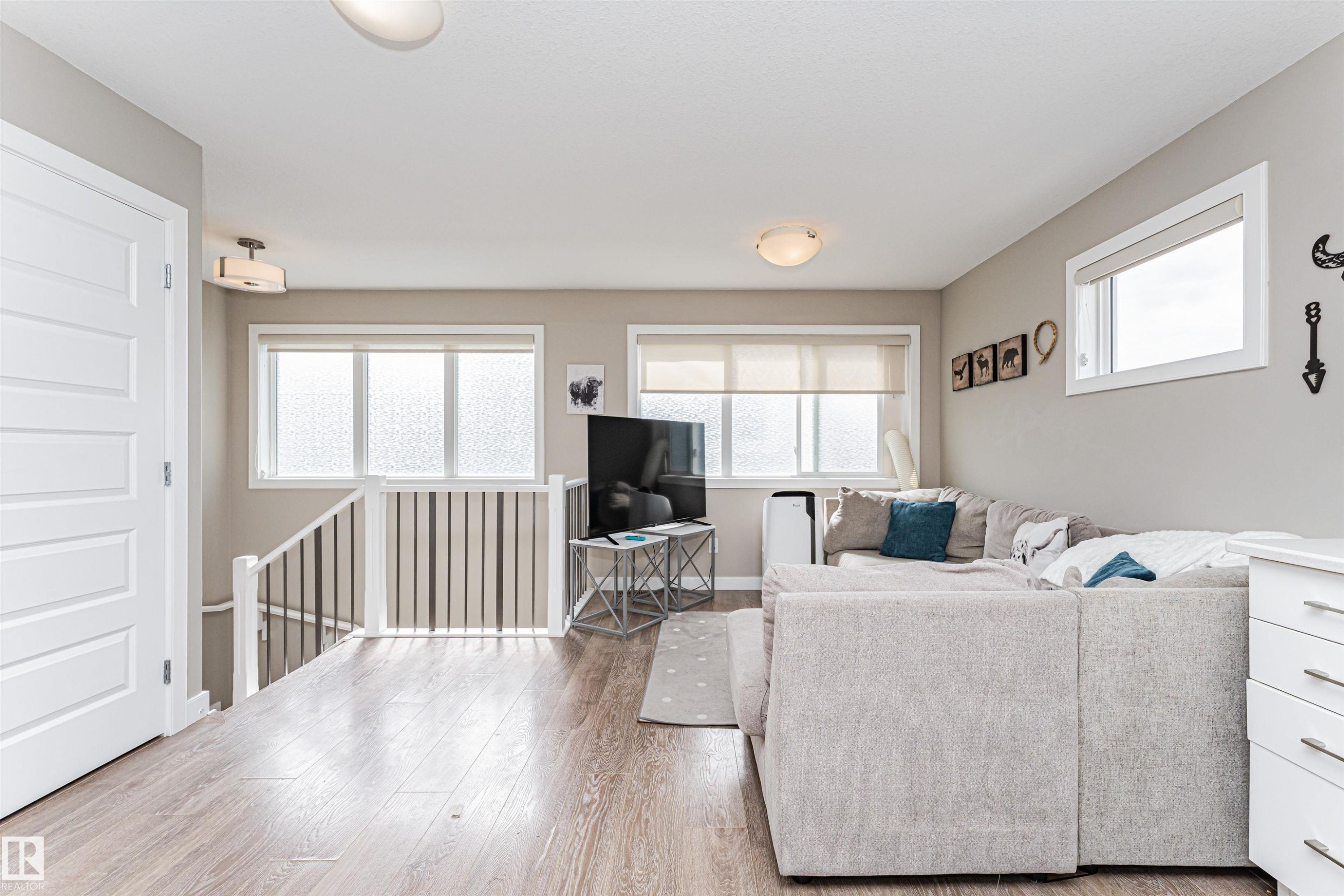 Spacious open-concept area featuring wood-finish flooring, multiple windows with roller shades, a contemporary white interior door, and a staircase with white railings - 22124 85 Avenue Nw, Edmonton, AB - Indoor