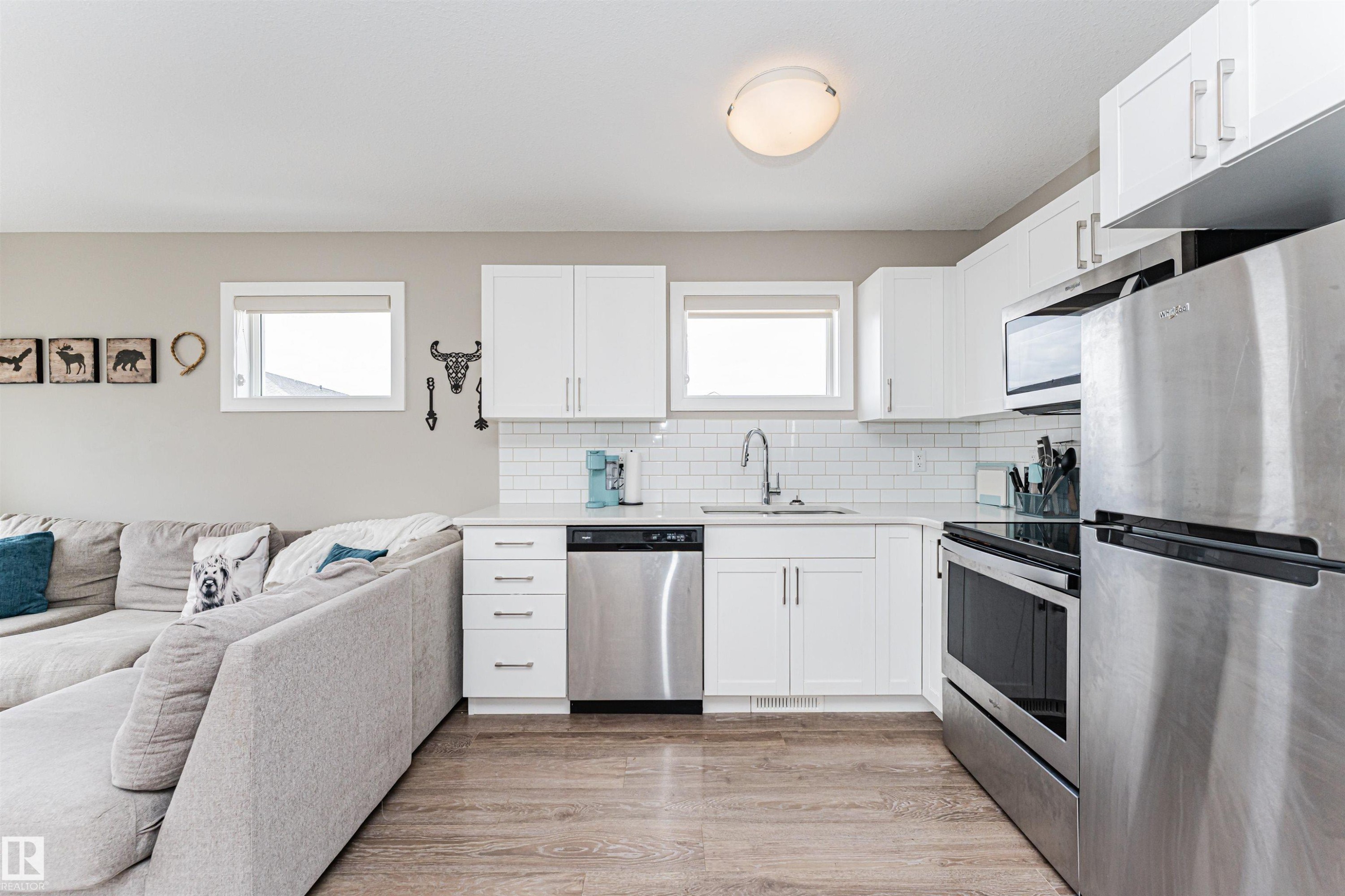 Open-concept living space featuring a kitchen with white cabinetry, stainless steel appliances, a subway tile backsplash, and a white countertop - 22124 85 Avenue Nw, Edmonton, AB - Indoor Photo Showing Kitchen With Stainless Steel Kitchen