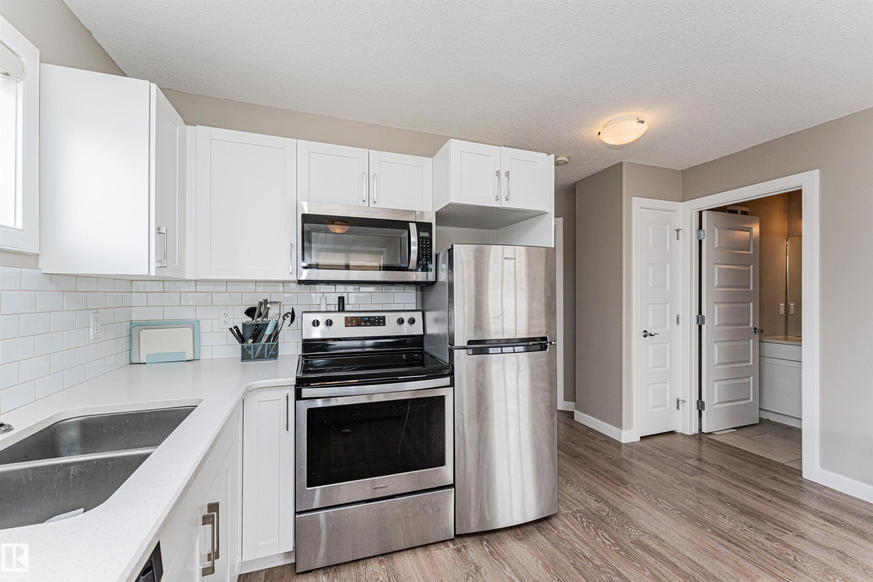 Kitchen featuring white cabinetry, stainless steel appliances, white subway tile backsplash, white countertops, and wood-finish flooring - 22124 85 Avenue Nw, Edmonton, AB - Indoor Photo Showing Kitchen With Stainless Steel Kitchen With Double Sink