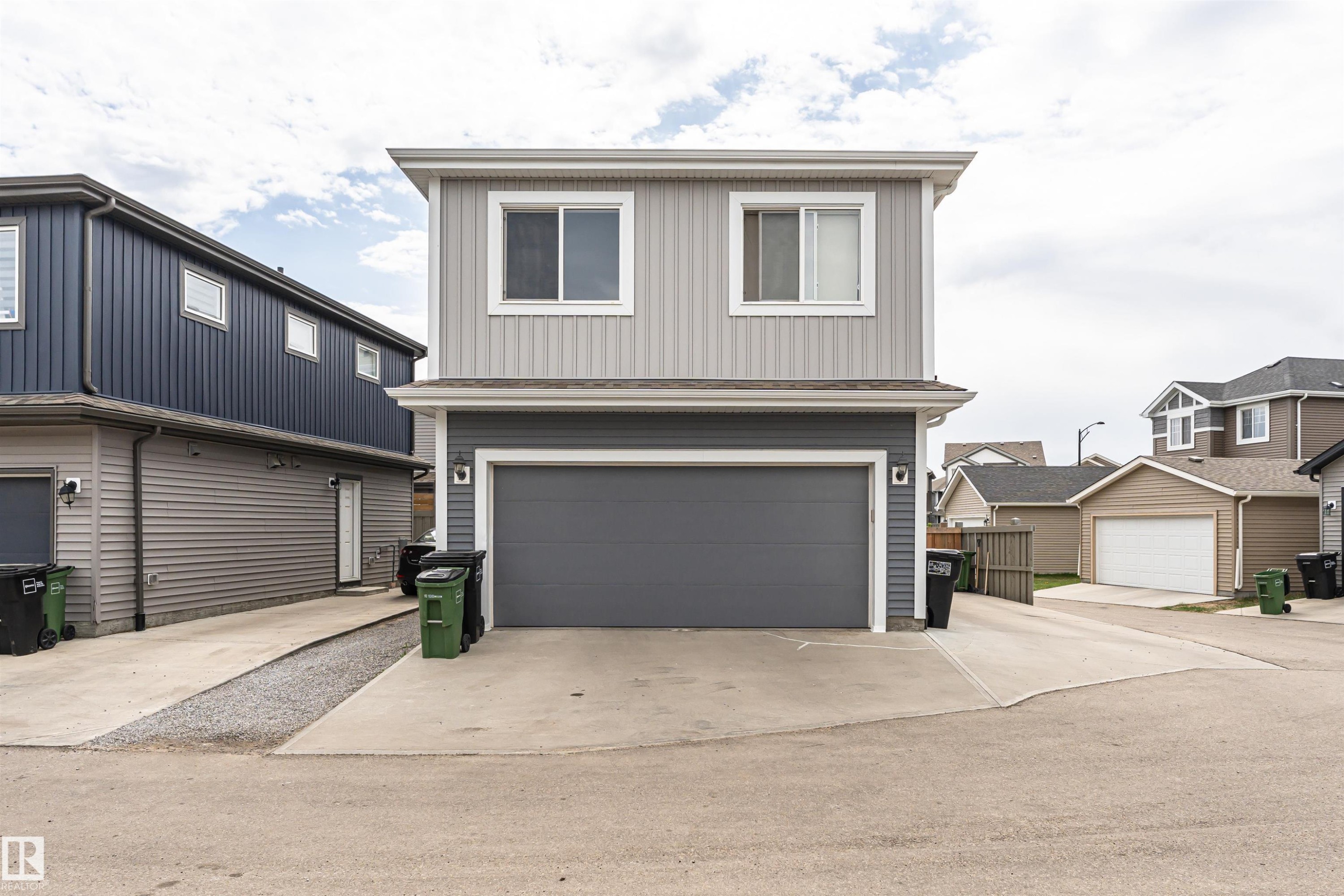 Two-story exterior with light gray vertical siding and horizontal dark gray siding, featuring a dark gray garage door, white framed windows, and a concrete driveway - 22124 85 Avenue Nw, Edmonton, AB - Outdoor With Exterior