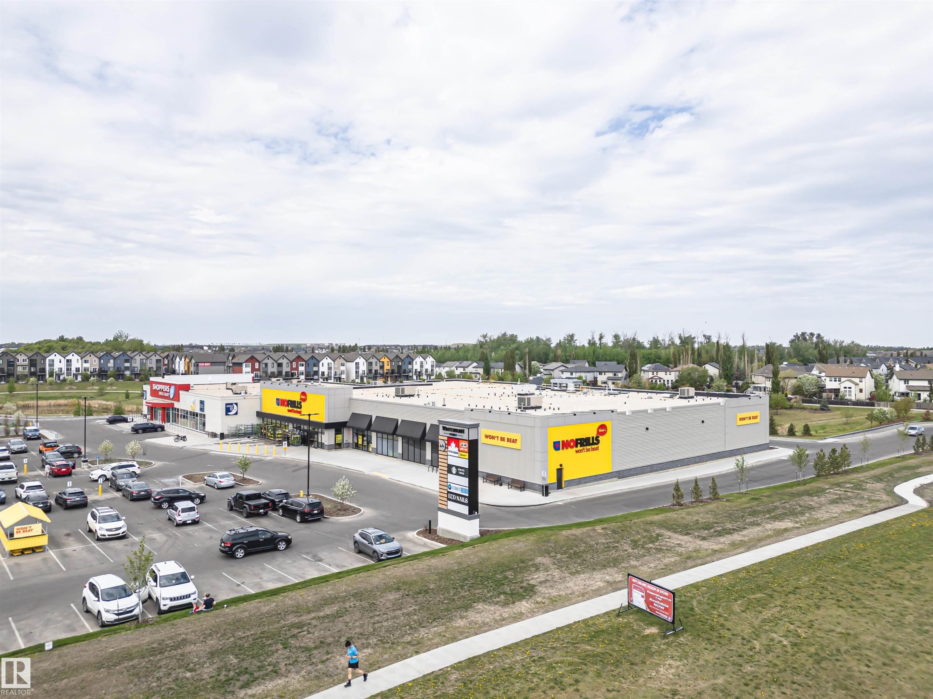 Commercial retail center featuring a large asphalt parking lot, multiple storefronts with black awnings, and prominent signage - 22124 85 Avenue Nw, Edmonton, AB - Outdoor With View