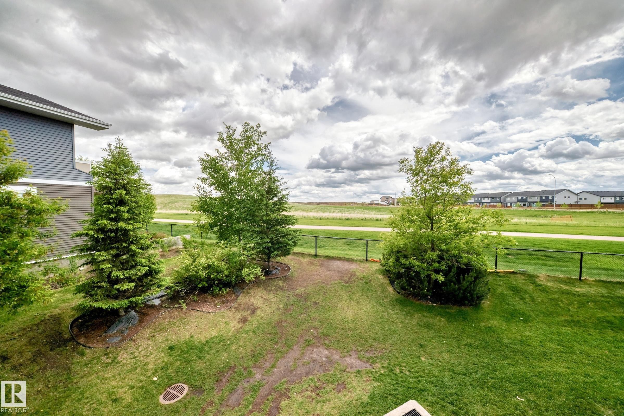 Expansive rear yard featuring green lawn, mature trees, and a black metal fence - 215 1510 Watt Drive, Edmonton, AB