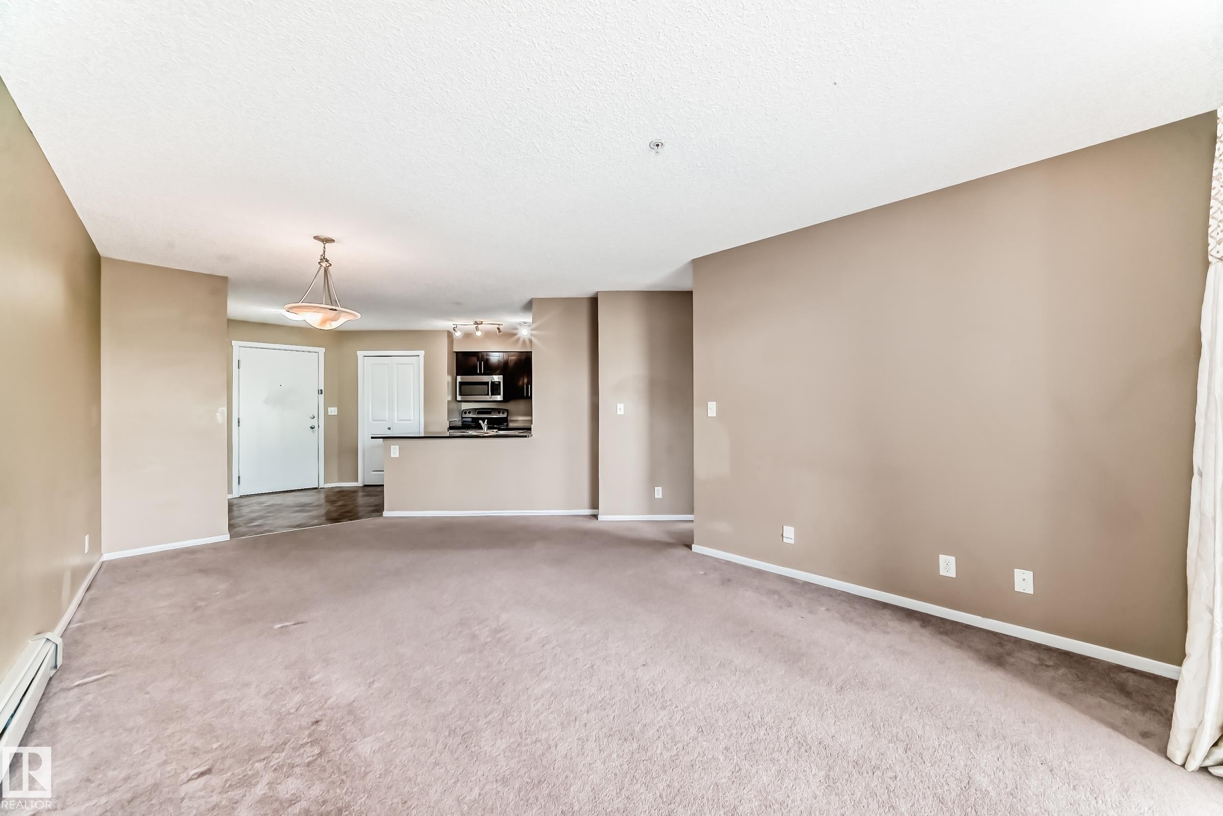 Open concept living area with neutral carpeting and warm beige wall tones - 215 1510 Watt Drive, Edmonton, AB