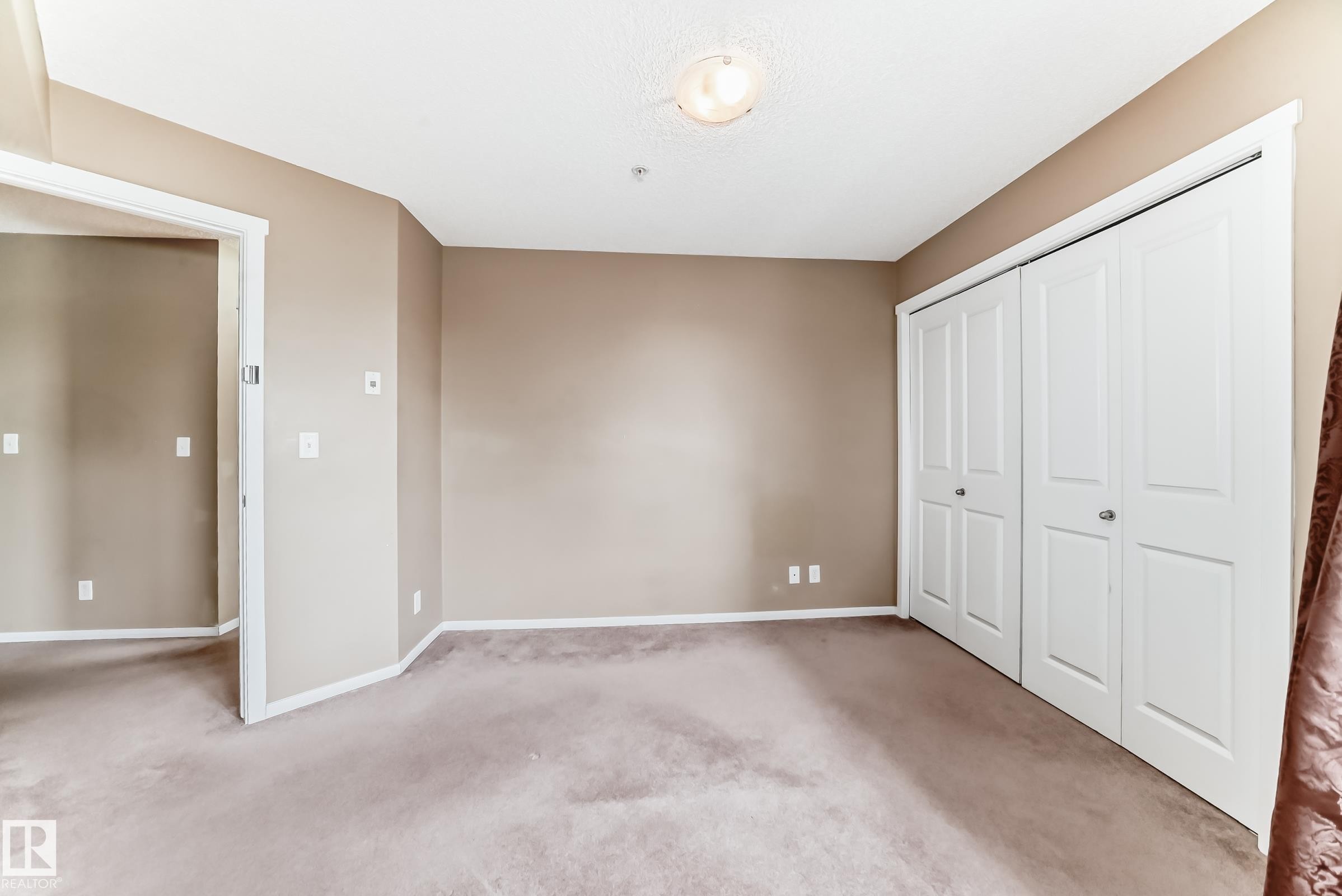 Carpeted room with neutral-toned walls, white trim, and a ceiling light fixture - 215 1510 Watt Drive, Edmonton, AB