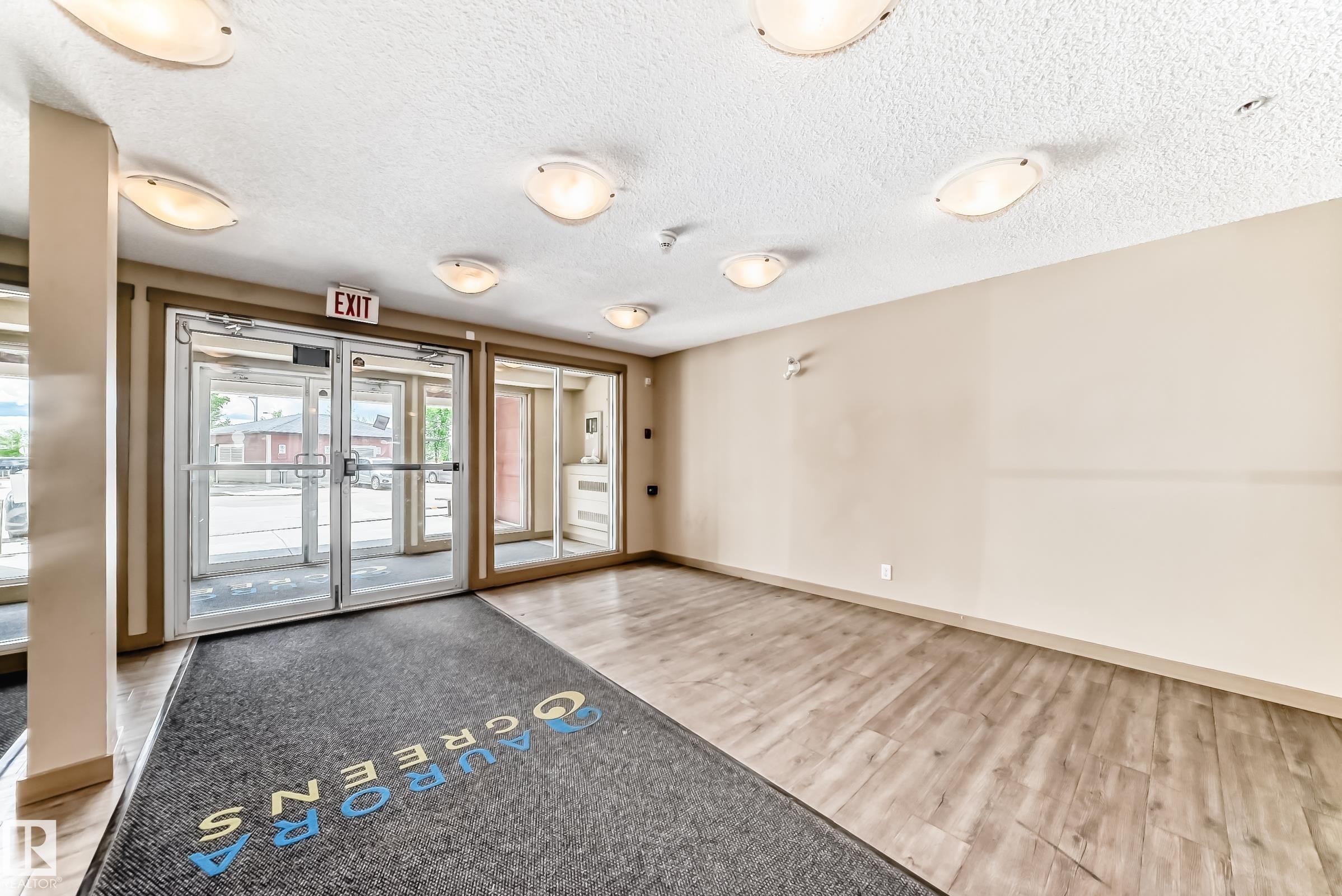Spacious common area featuring light-toned walls, wood-finish flooring, and multiple ceiling-mounted light fixtures - 215 1510 Watt Drive, Edmonton, AB