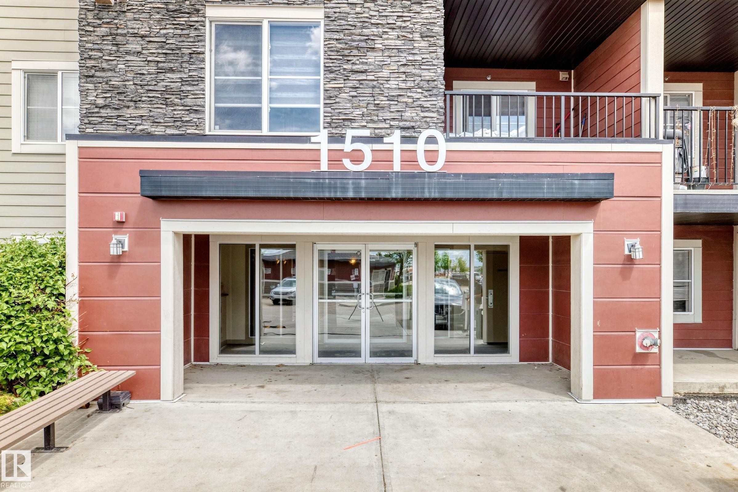 Building entrance featuring a stacked stone facade and horizontal siding - 215 1510 Watt Drive, Edmonton, AB